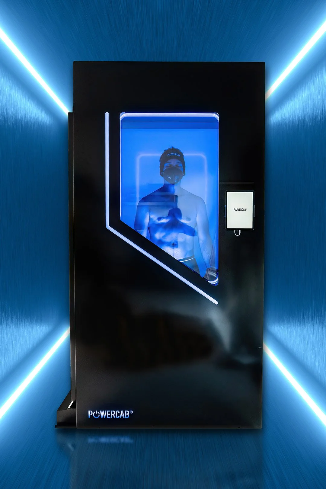 A person inside a blue lighted cryotherapy chamber wearing a face mask and minimal clothing, with the word 'POWERCAB' on their headband, in a futuristic setting.