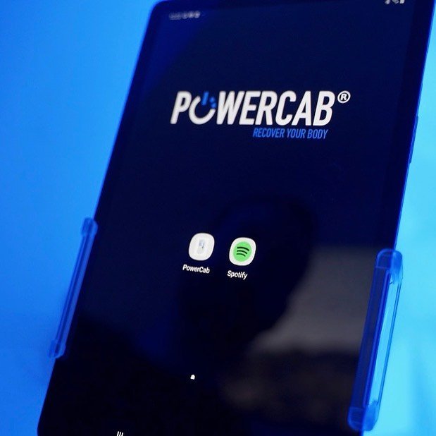 A smartphone in a blue phone holder displaying a PowerCab app and a Spotify app on its screen.