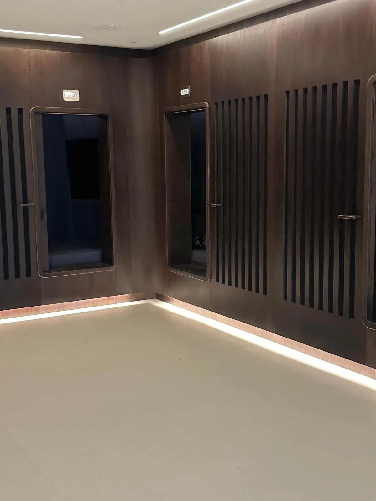 Interior space with dark wooden wall panels, two elevator doors, and subtle lighting along the ceiling and floor.