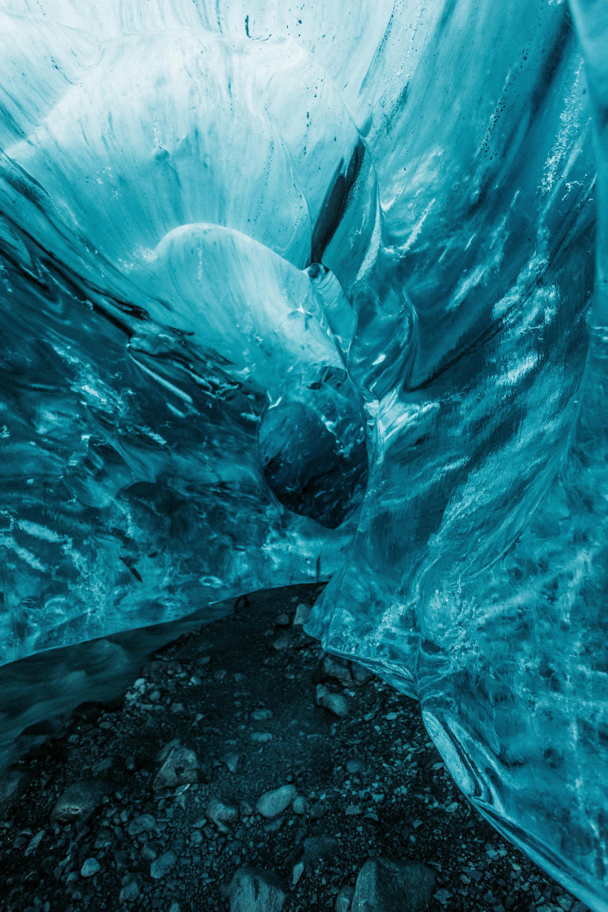 Close-up of a glacier's icy entrance with blue ice walls and rocky ground.