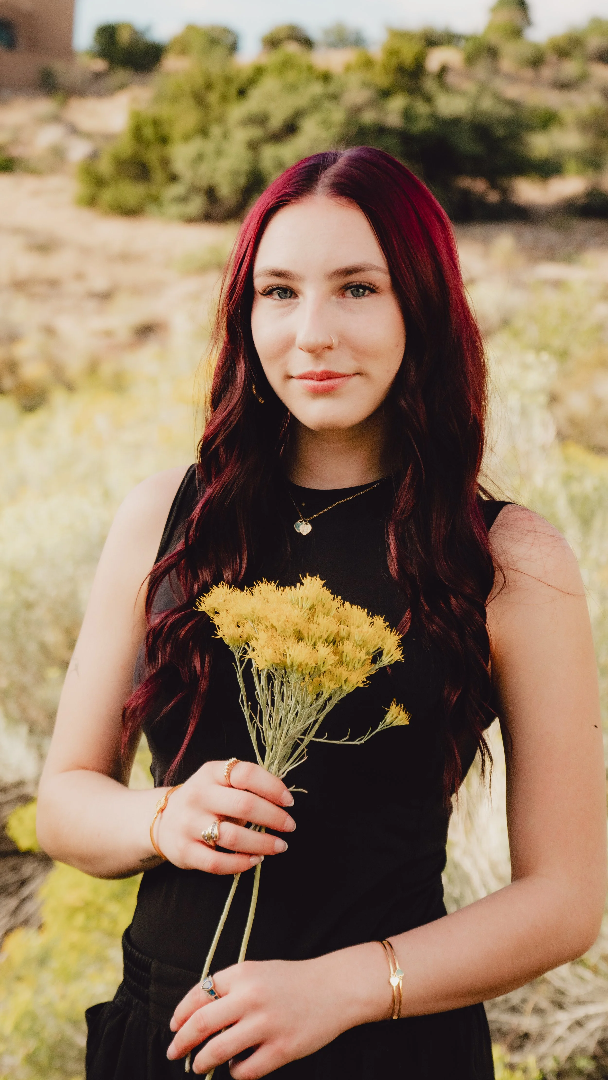 A young woman with red hair holding yellow flowers outdoors in a natural setting.