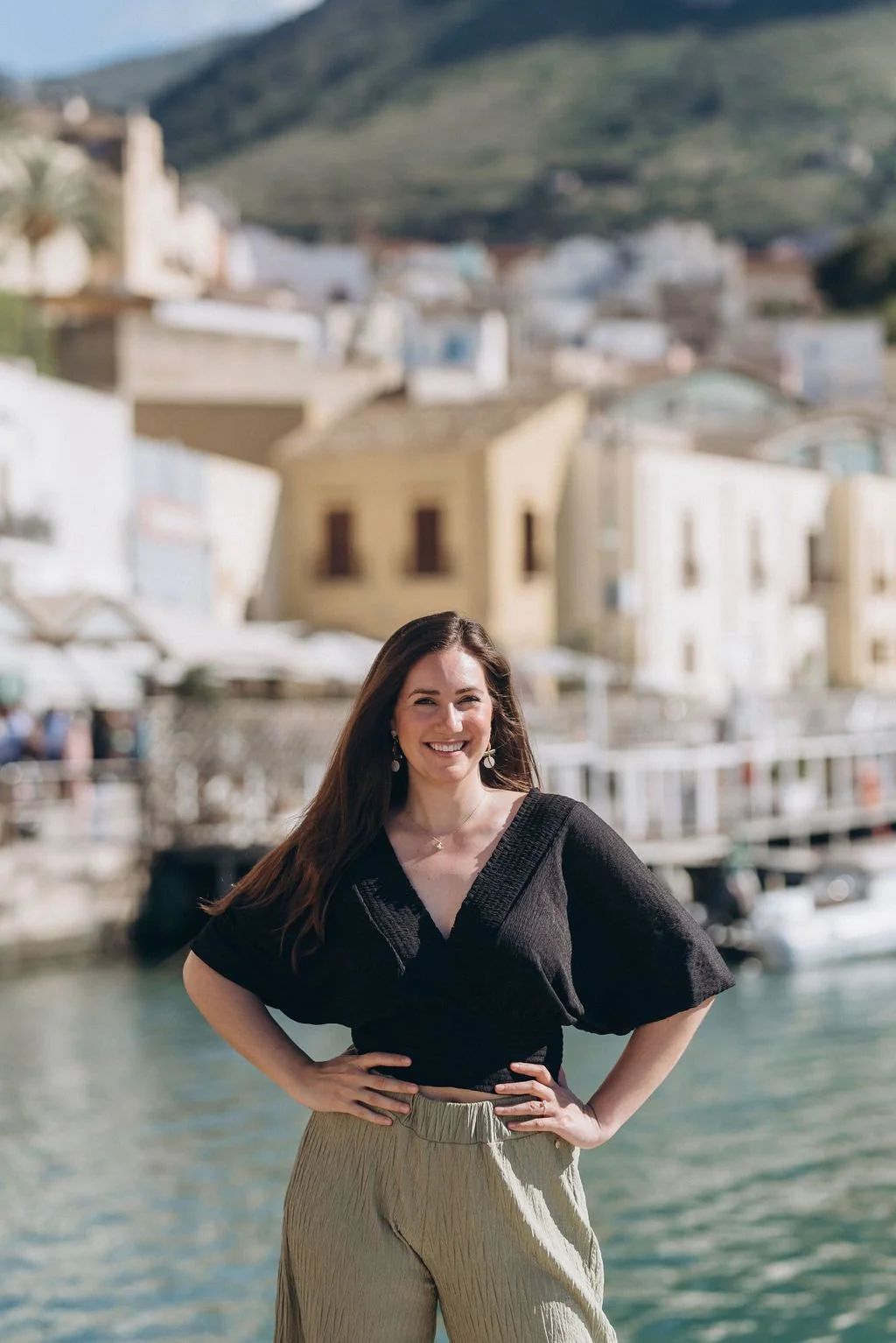 Mackenzie Fly is posing with her hands on her hips with a Sicilian city as the backdrop