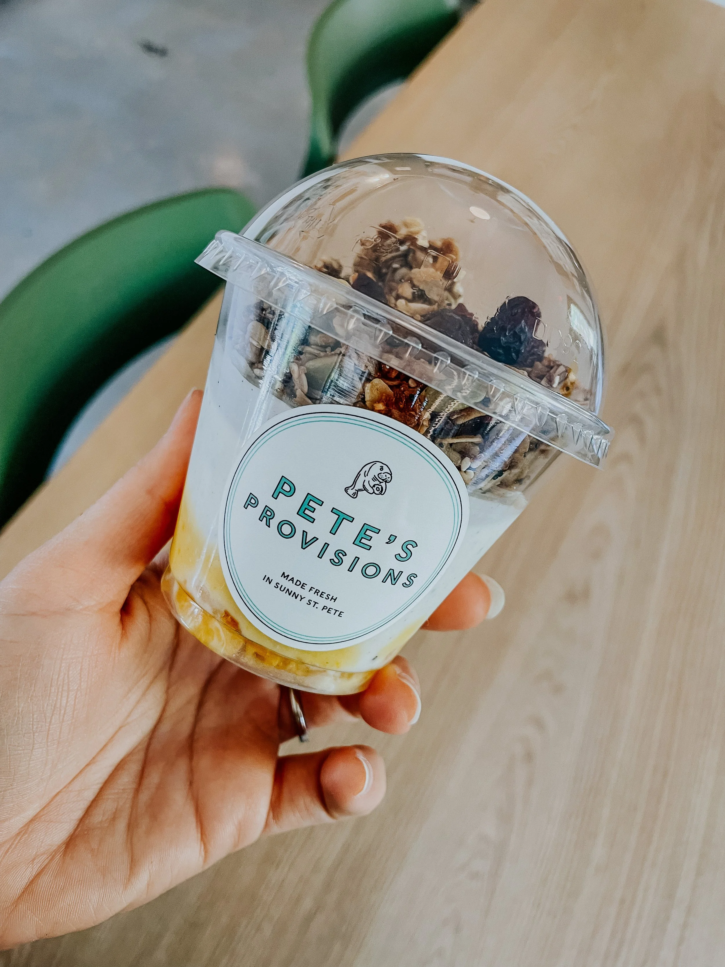 A hand holding a Pete's Provisions yogurt parfait with granola and fruit, labeled "Made Fresh in Sunny St. Pete."