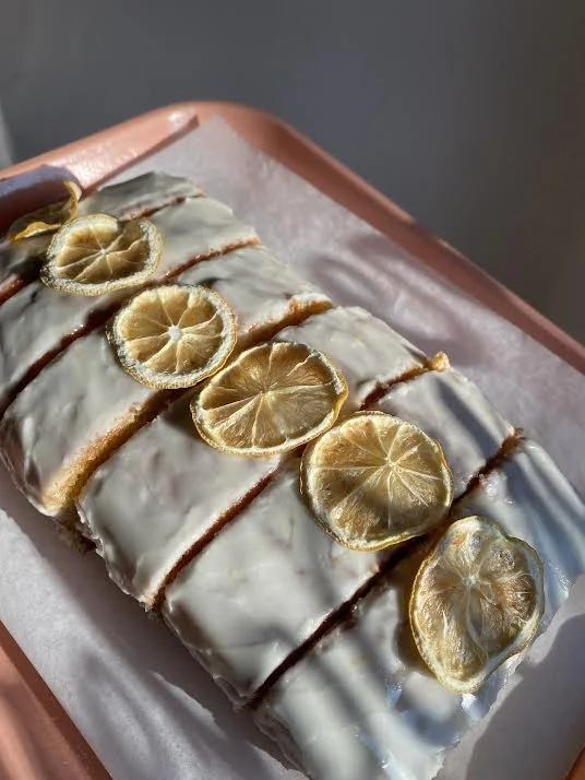 Sliced lemon loaf cake with glaze and dehydrated lemon slices on top, arranged on a parchment-lined tray.