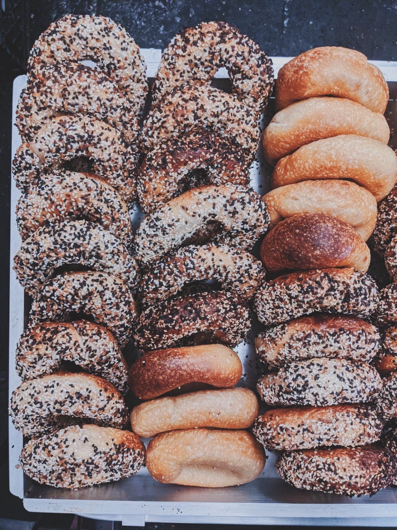 Assorted bagels, some with seeds, displayed on a baking tray.