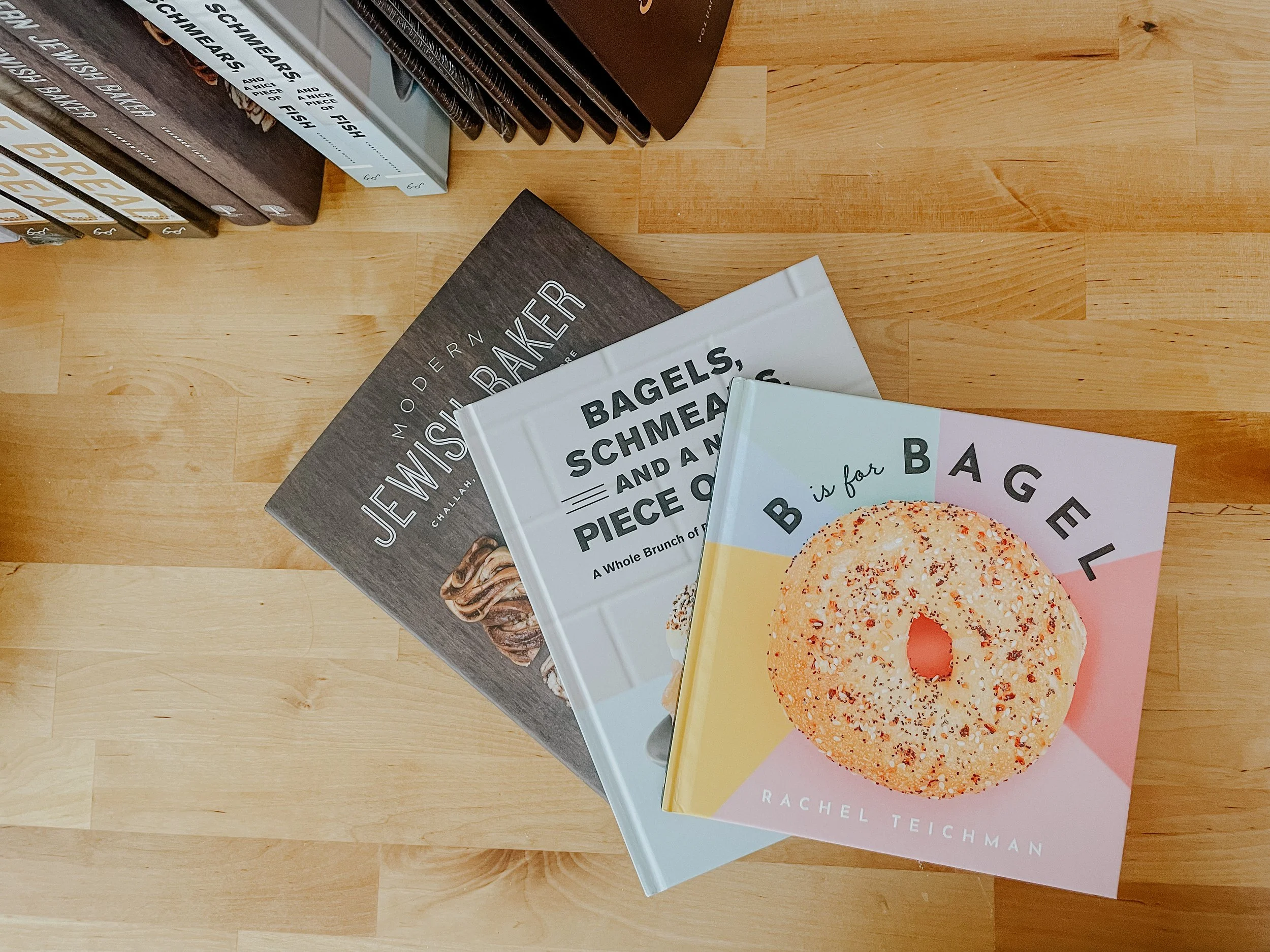 Three books on baking and bagels on a wooden table, including "B is for Bagel."