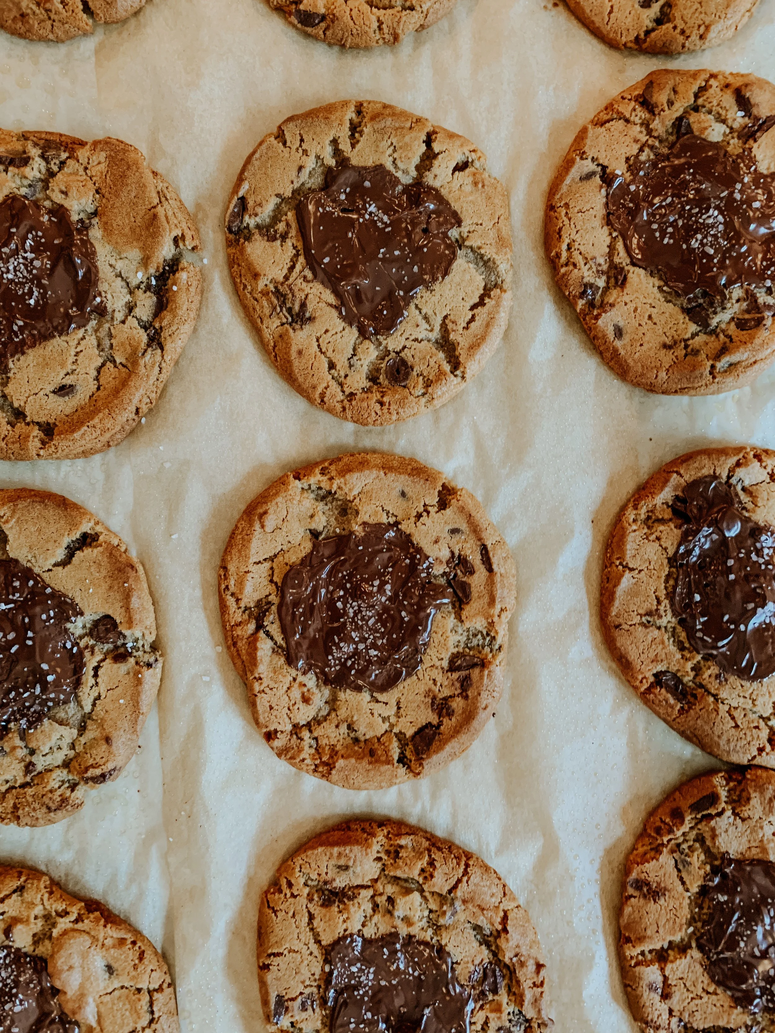 Chocolate chip cookies with melted chocolate and sea salt on parchment paper.