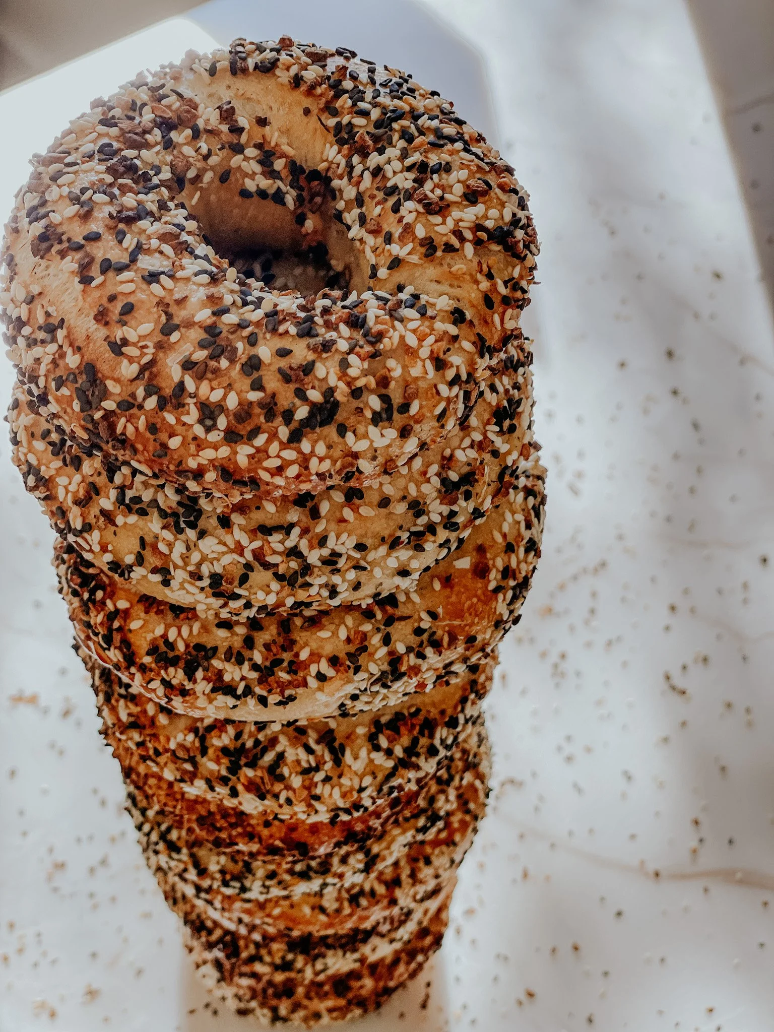Stack of everything bagels with sesame and poppy seeds on a white surface.