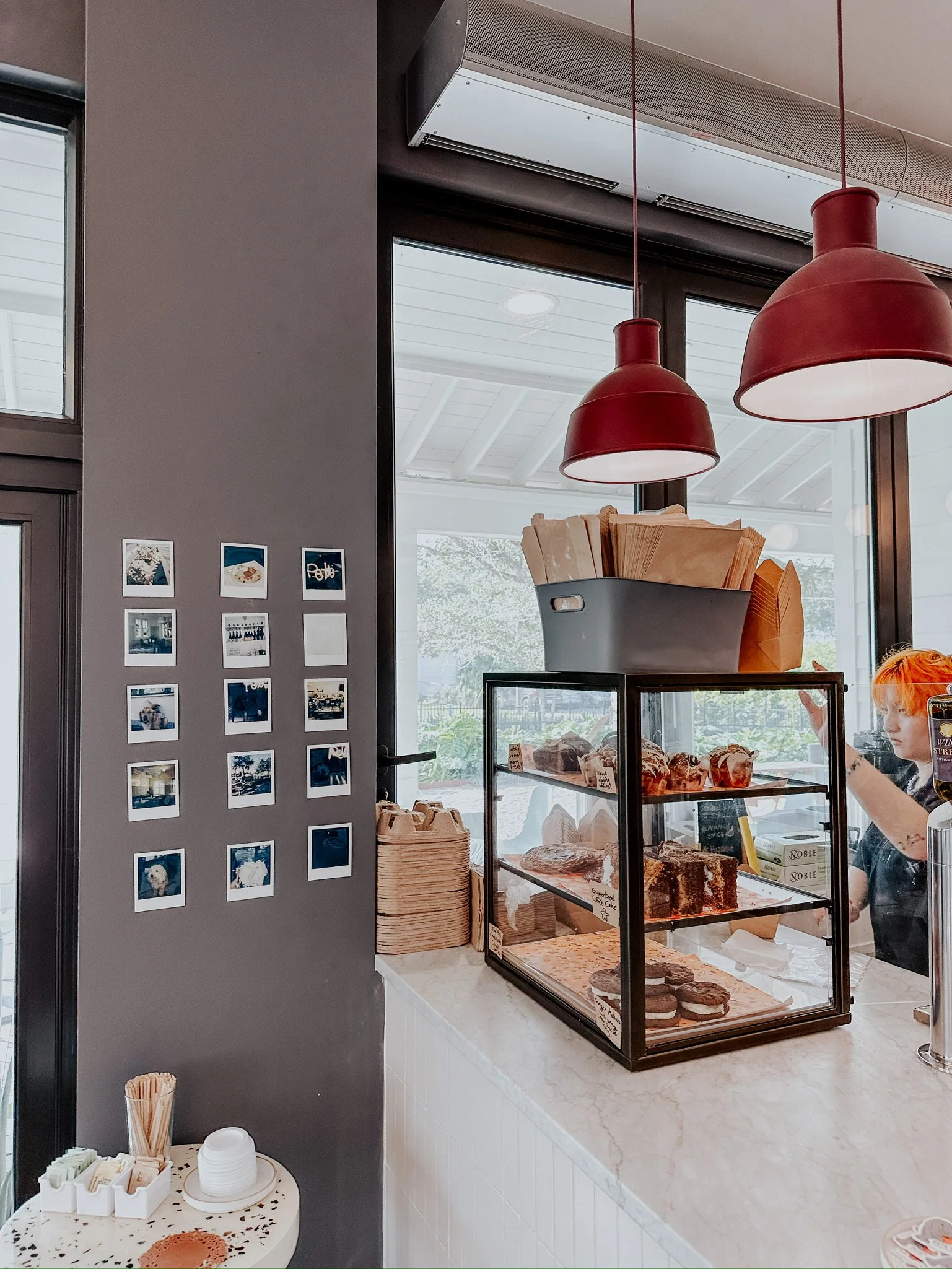Coffee shop counter with bakery display case and polaroid photos on the wall.