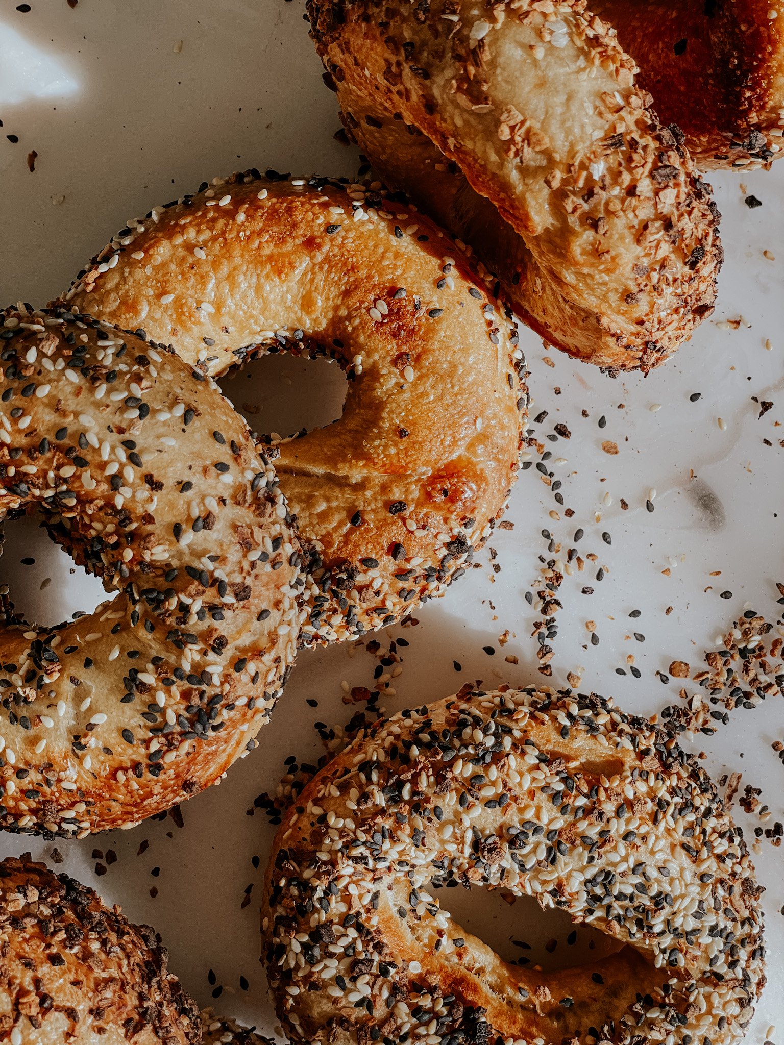 Freshly baked everything bagels with sesame and poppy seeds on a white surface.