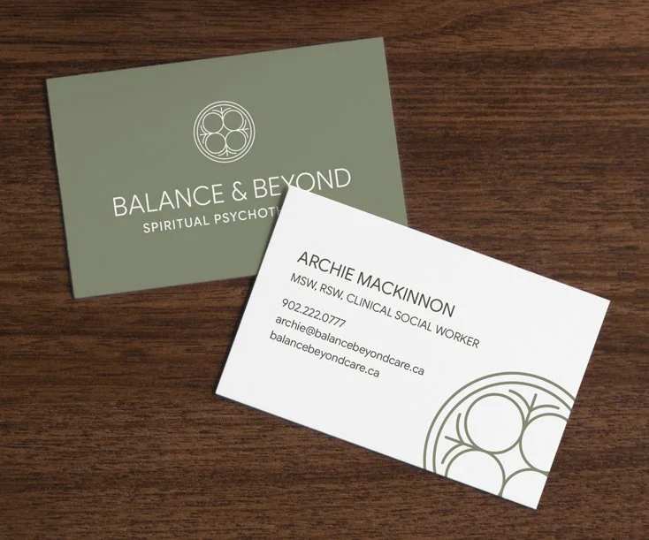 Business cards for Balance & Beyond Spiritual Psychotherapy and Archie Mackinnon, a clinical social worker, on a wooden surface.