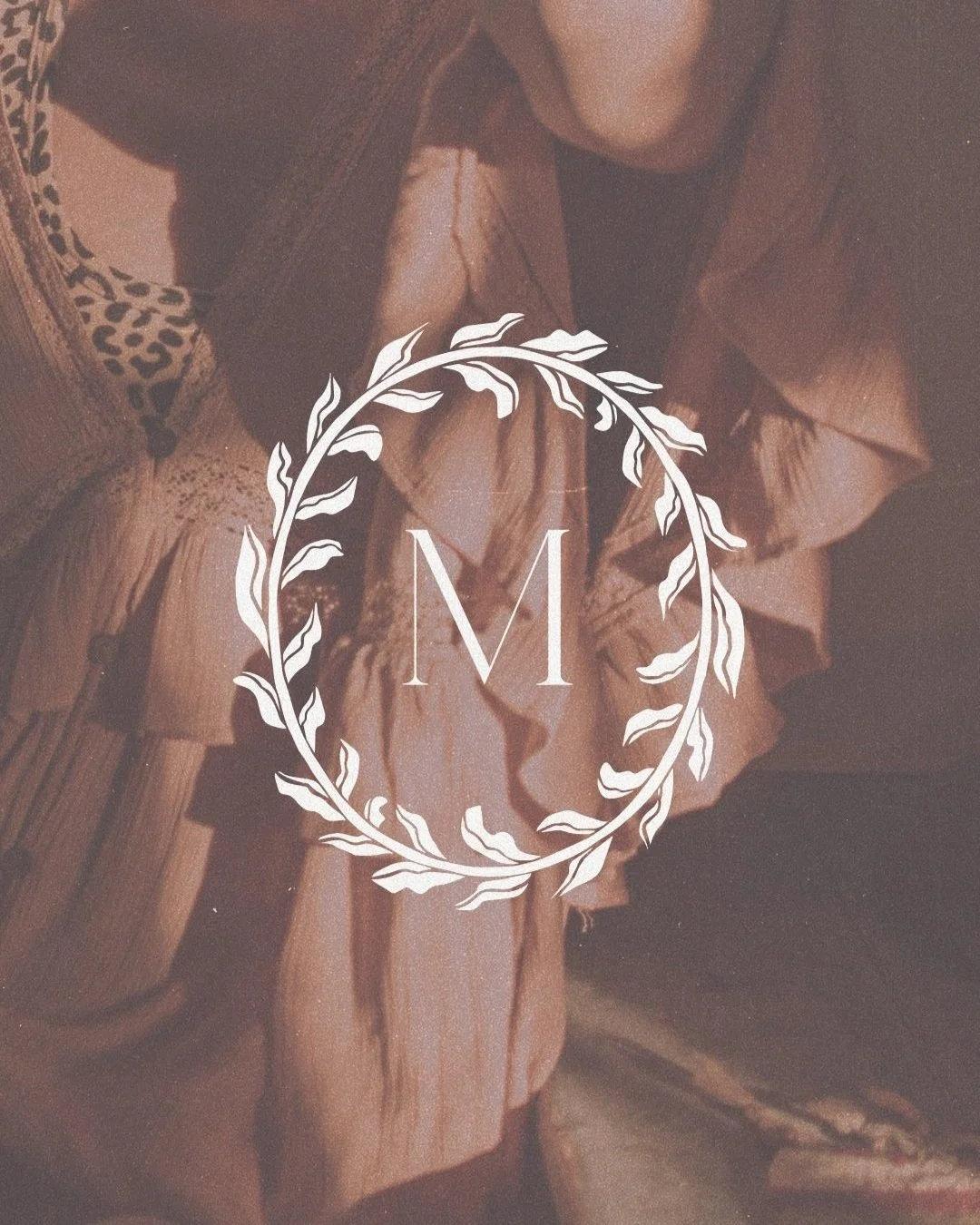 A monogram with the letter 'M' surrounded by a decorative wreath overlaying a background of fabric and wood textures.