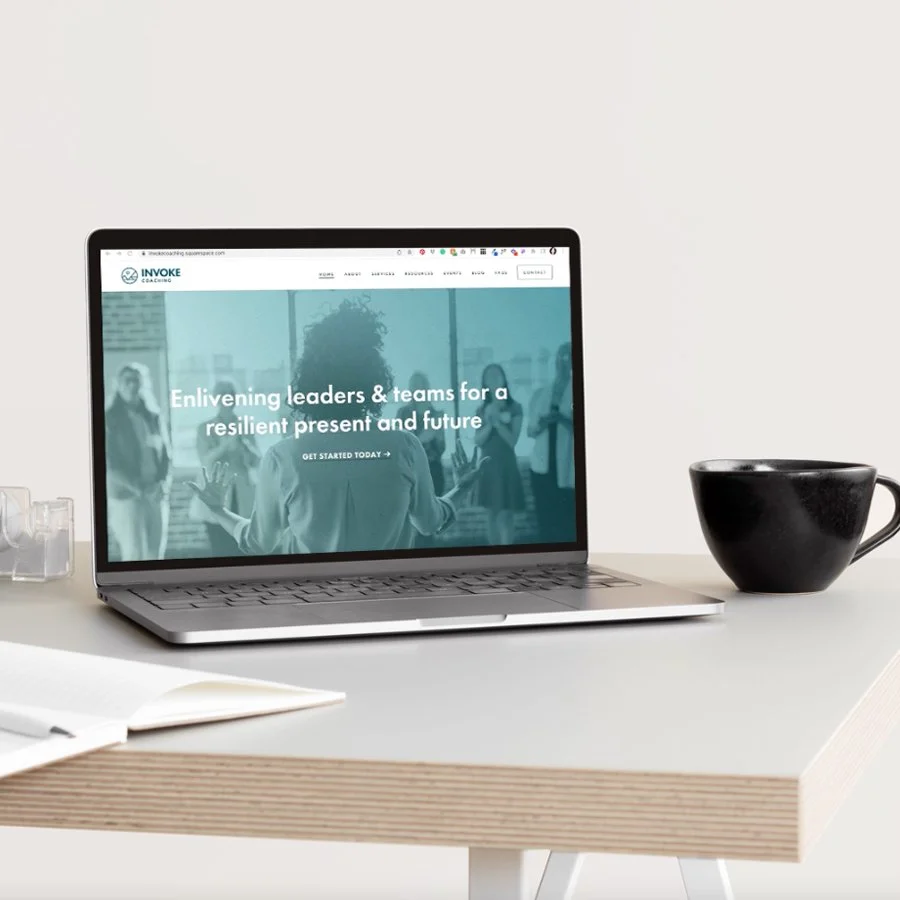 Laptop on desk displaying Invoke Coaching website with the slogan 'Enlivening leaders & teams for a resilient present and future'