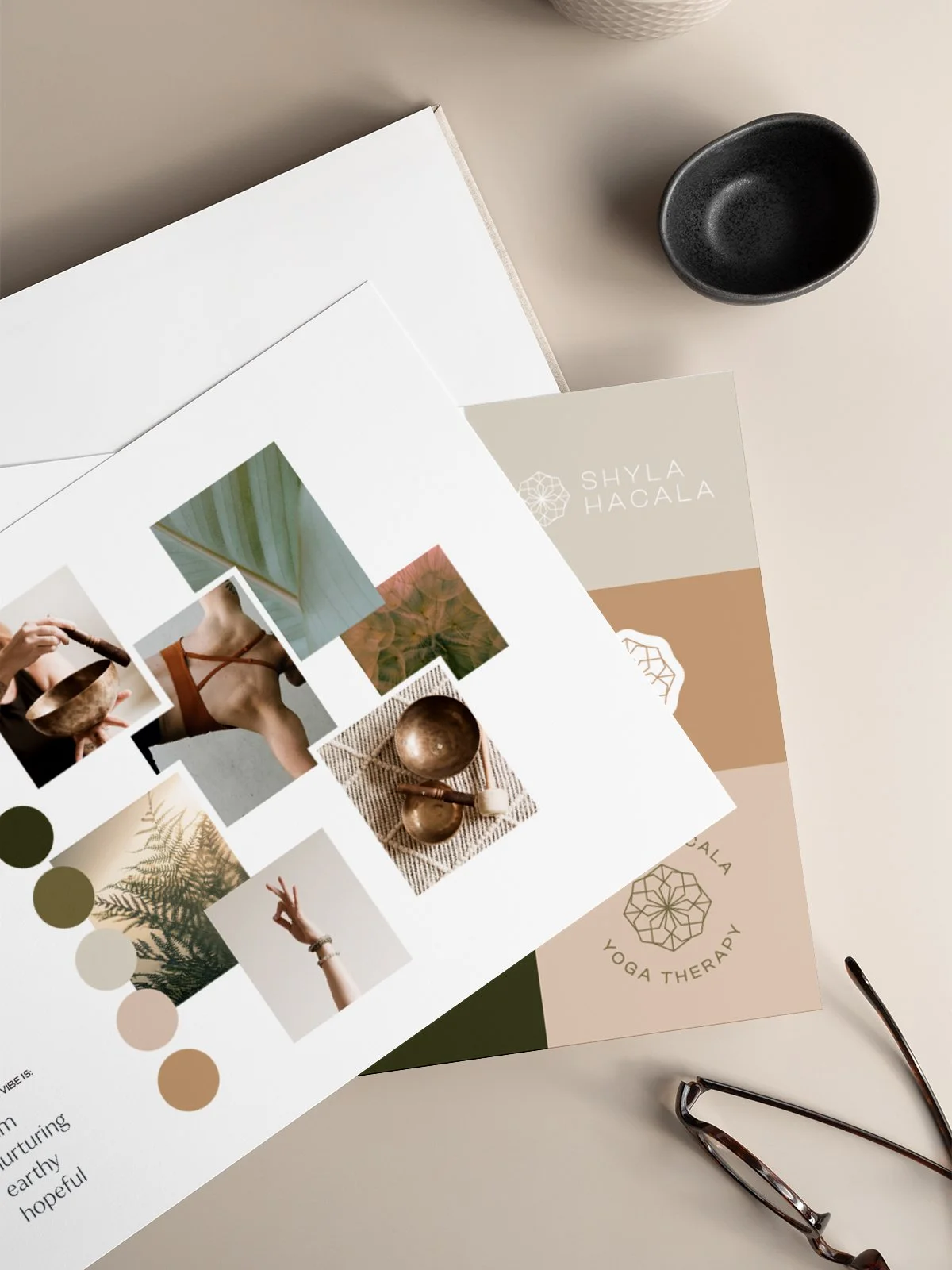 Open design palette with earthy, neutral colors, photos, and swatches alongside a yoga therapy brochure, black bowl, and reading glasses.