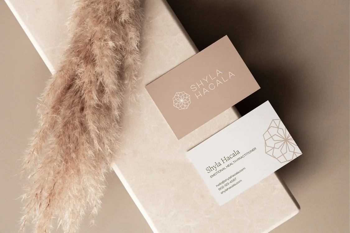 Business cards and a beige box, with a fluffy beige pampas grass stem on the left, seen from above.