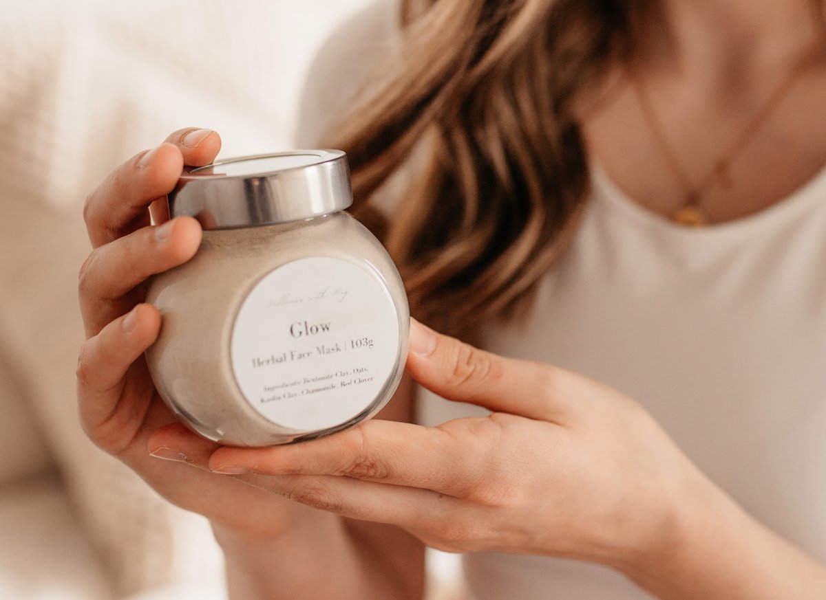 A woman holding a jar of skincare product labeled 'Glow Herbal Face Mask'.