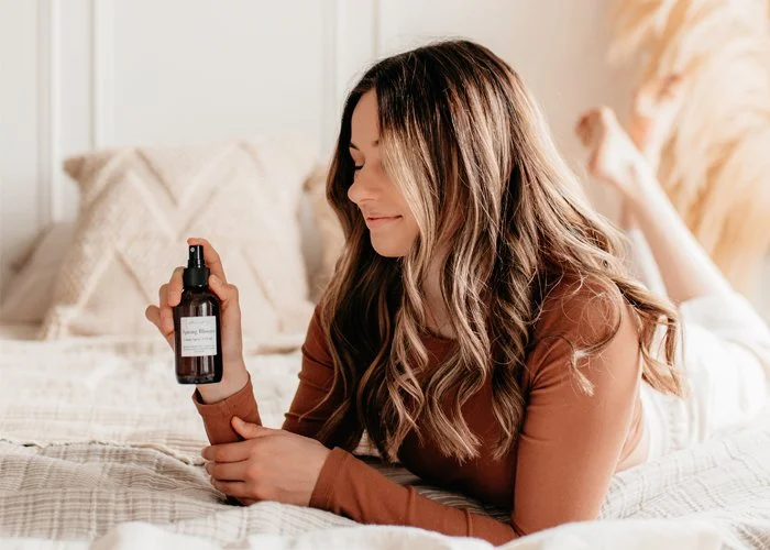 Woman lying on bed holding a spray bottle.