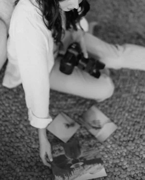 A person sitting on the ground looking at photographs spread out on the ground.