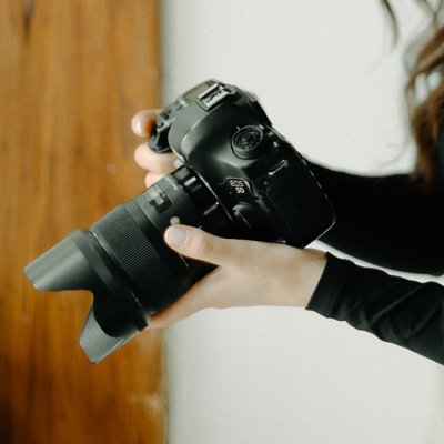 Person holding a black digital camera with a lens in their right hand.