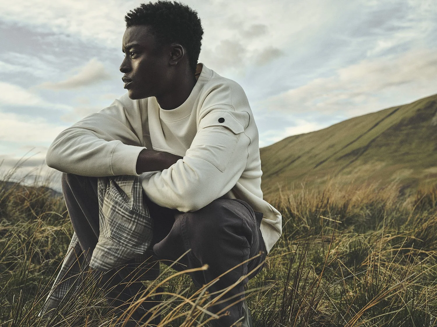 Dan Jackson photographs a male model for Barbour SS26, crouching in long grass in the  Scottish Highlands