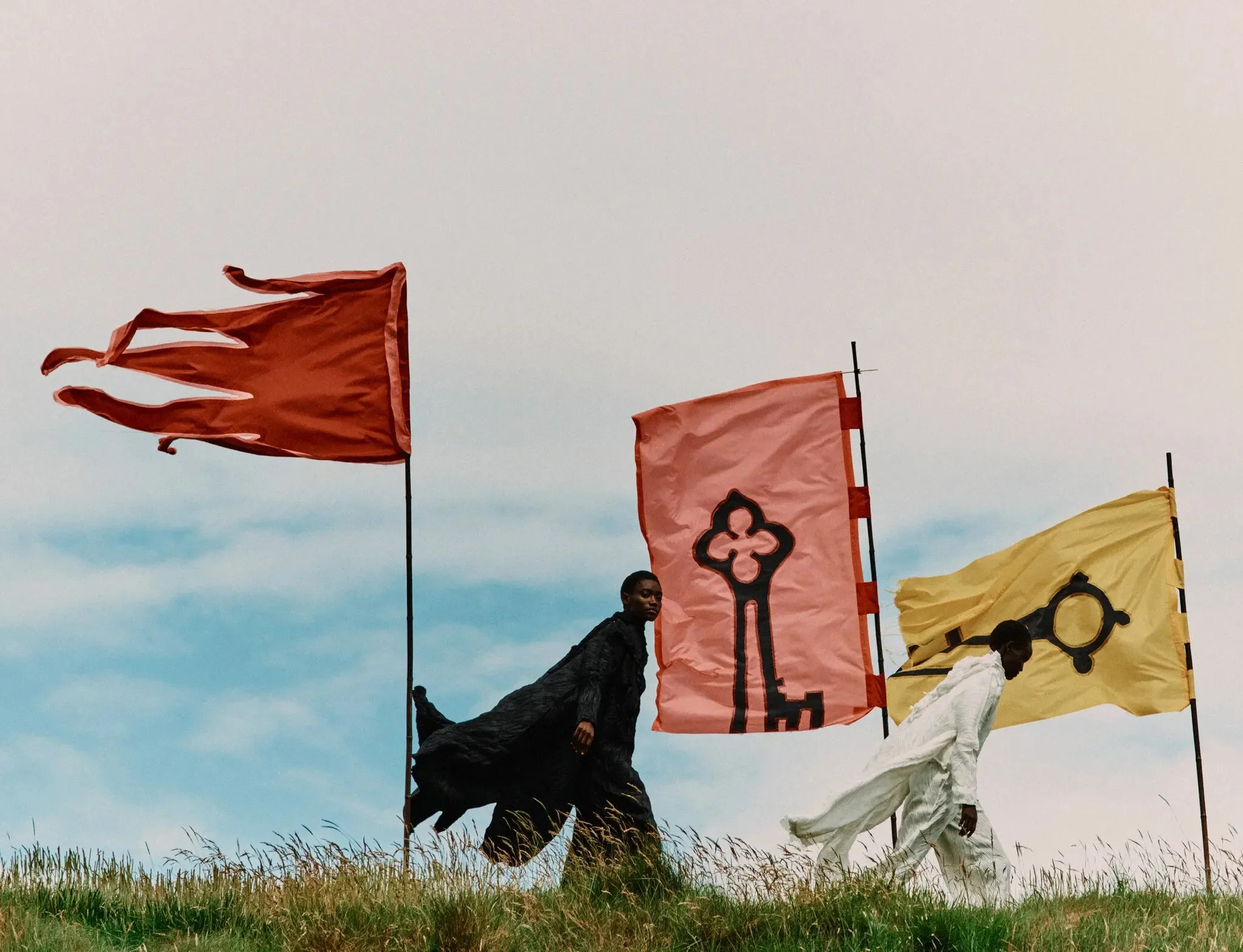 2 models photographed with flags by Jack Davison for T: The  New York Times Style Magazine. 
Models wear Issey Miyake coat, top, top (worn underneath) and pants. Issey Miyake coat, top, top (worn underneath) and pants.
Produced by Mini Title. Local P