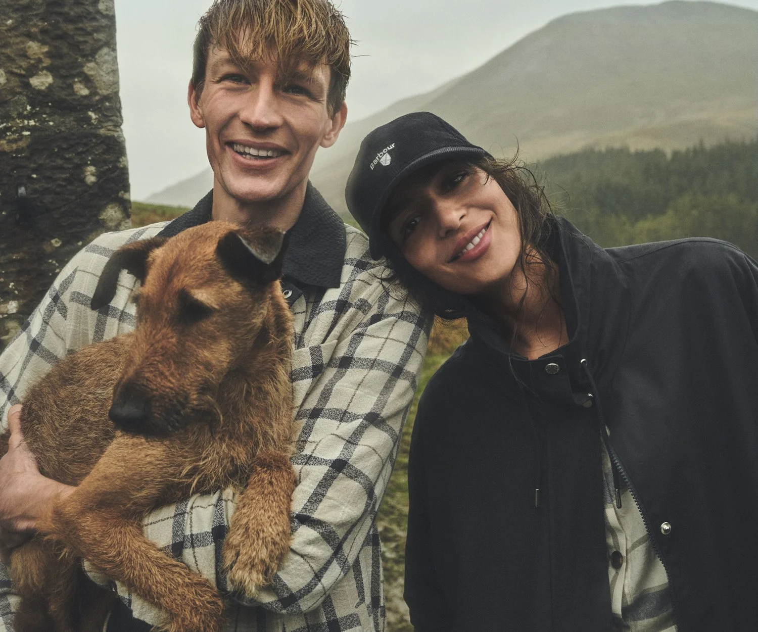Smiling models and a dog pose for photographer Dan Jackson in the rain while working in Scotland on the Barbour Spring/Summer 26 photoshoot