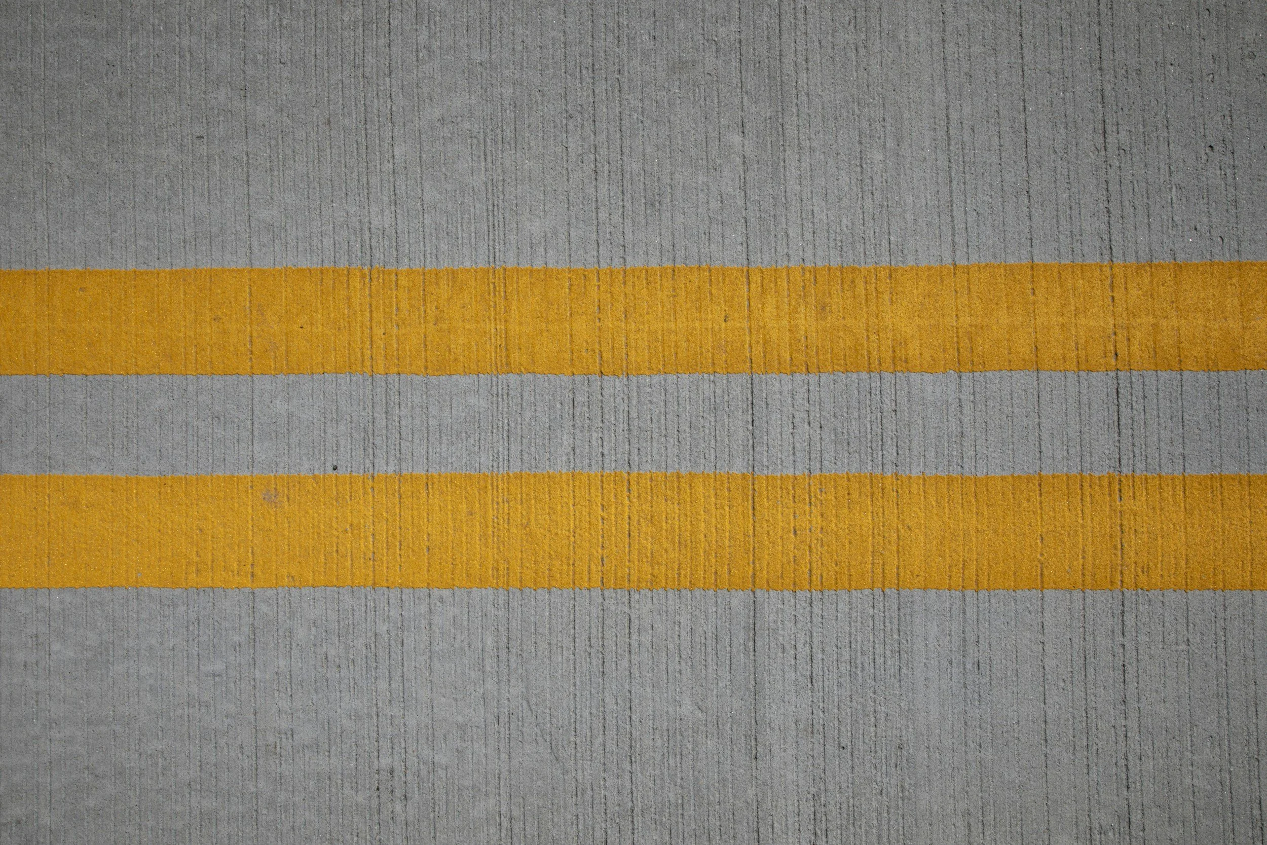 Close-up of a section of a sidewalk with a yellow painted line dividing it into two parts.