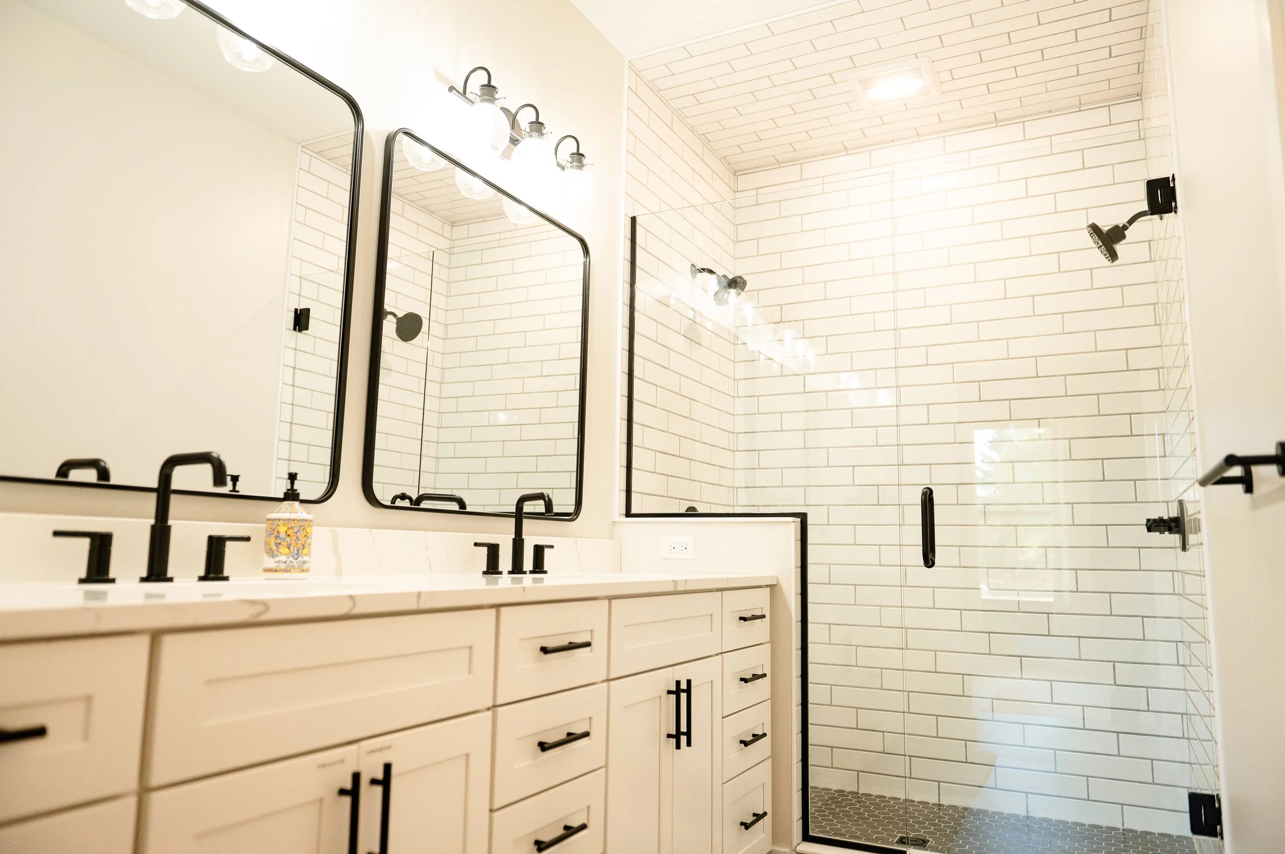 Modern bathroom with white cabinetry, black fixtures, large wall mirror, and a spacious walk-in shower with white subway tiles and a black-framed glass door.