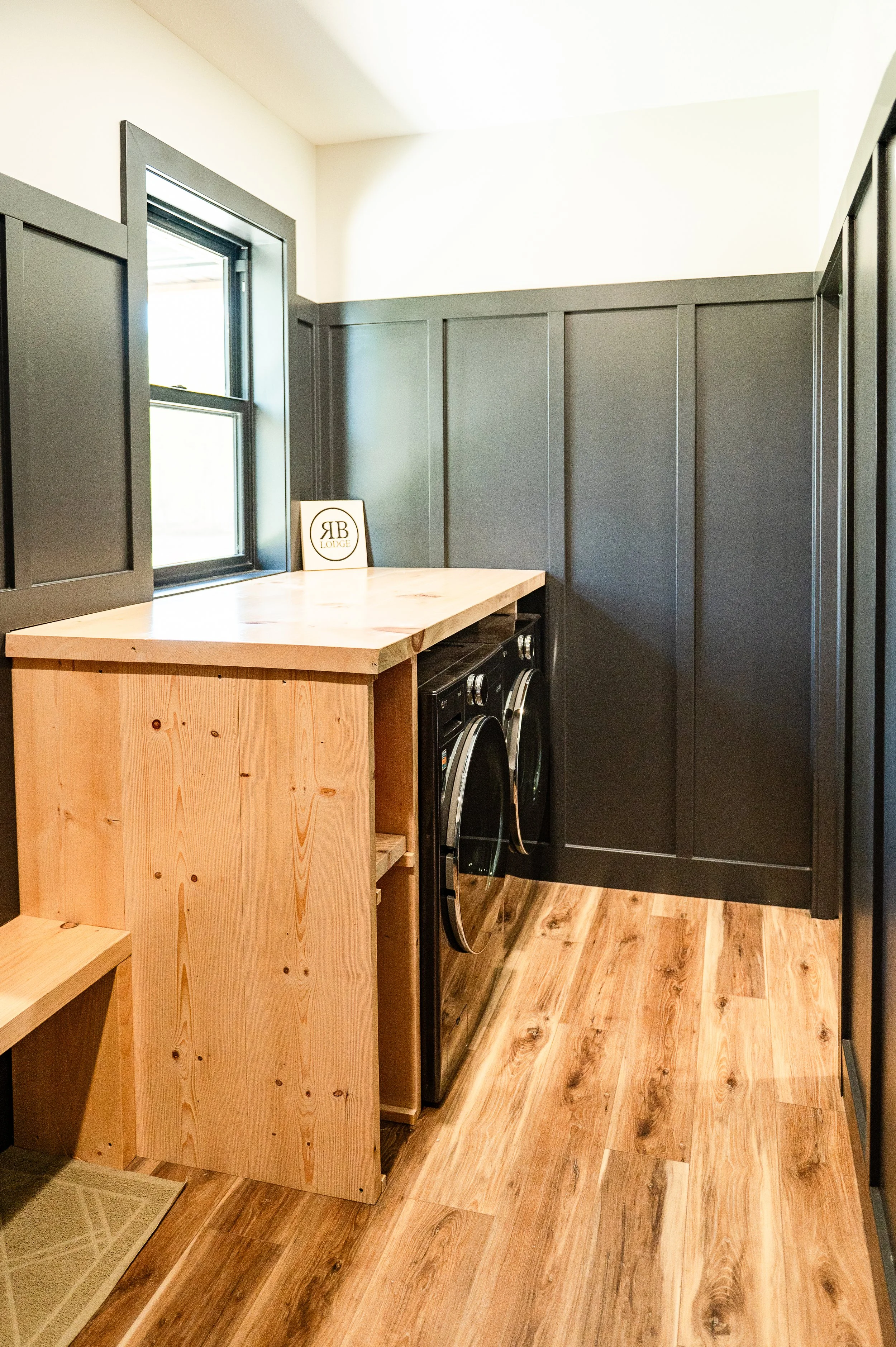 Small laundry room with wood flooring, dark gray wall cabinets, a wooden island, and a front-loading washer and dryer.