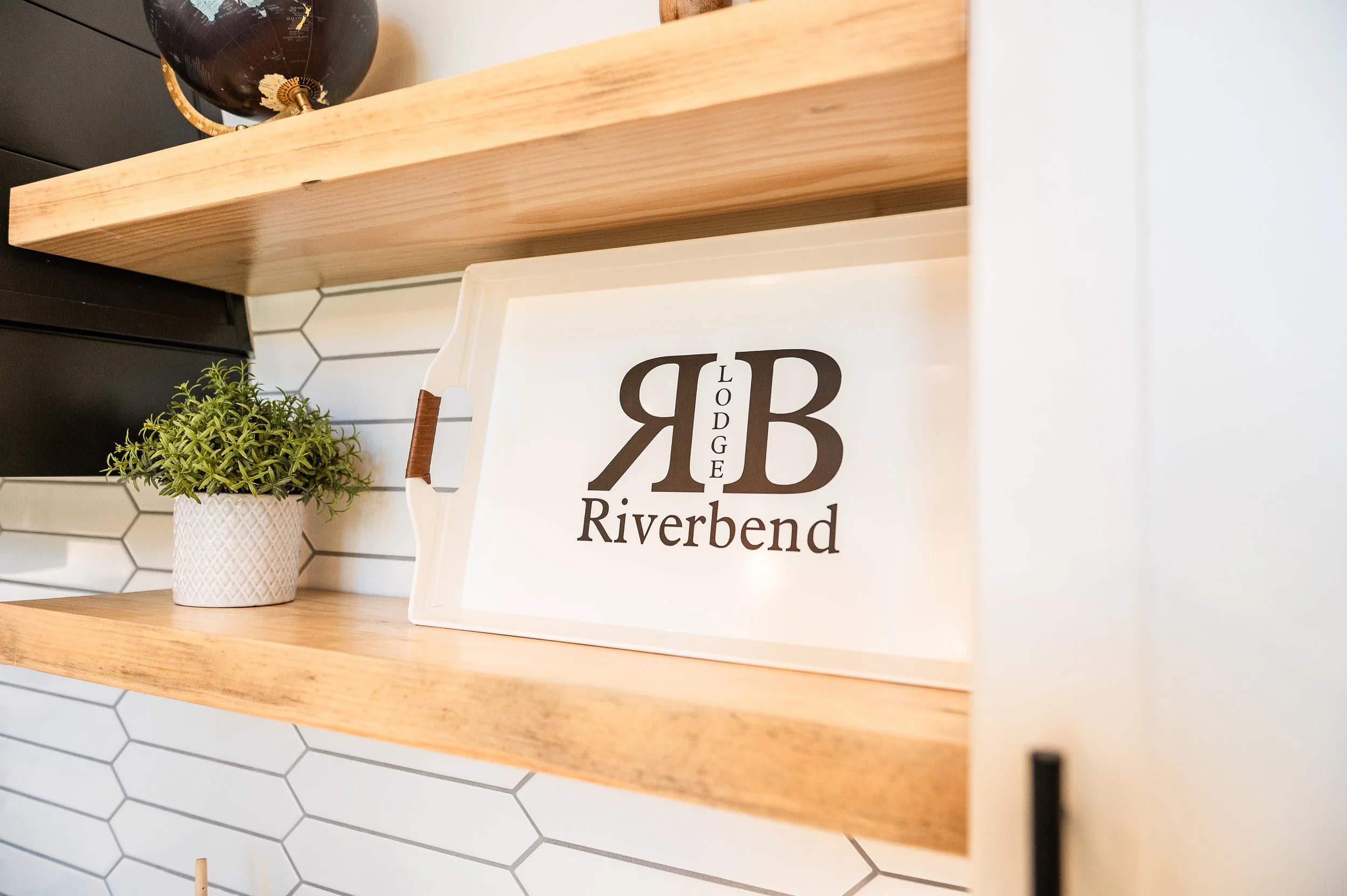 A wooden shelf with a globe on the left and a potted plant on the right. Behind the shelf, a sign reads 'BB RIVERBEND'.