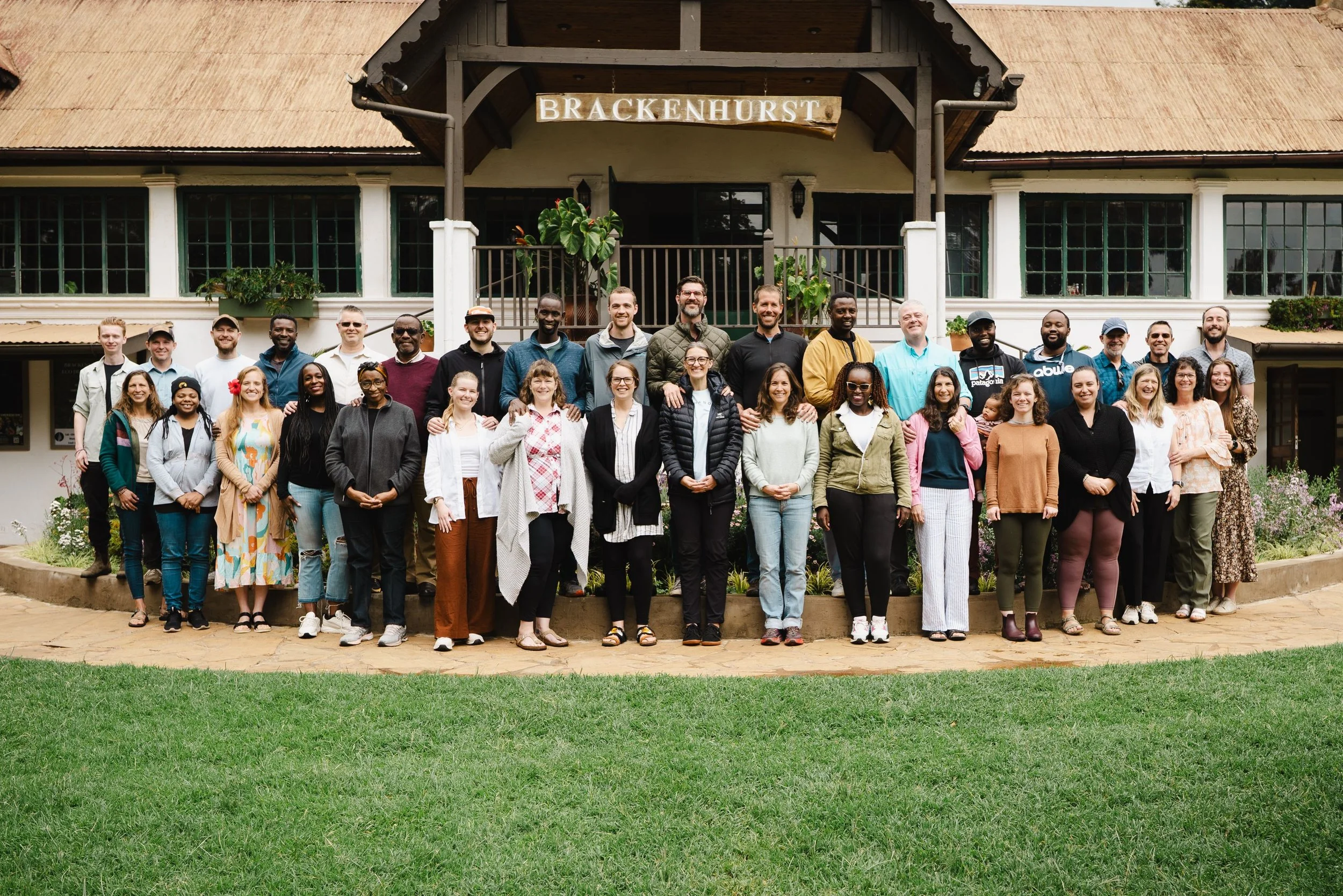 Group of diverse people standing in front of a building with a sign that reads 'Brackenhurst.'