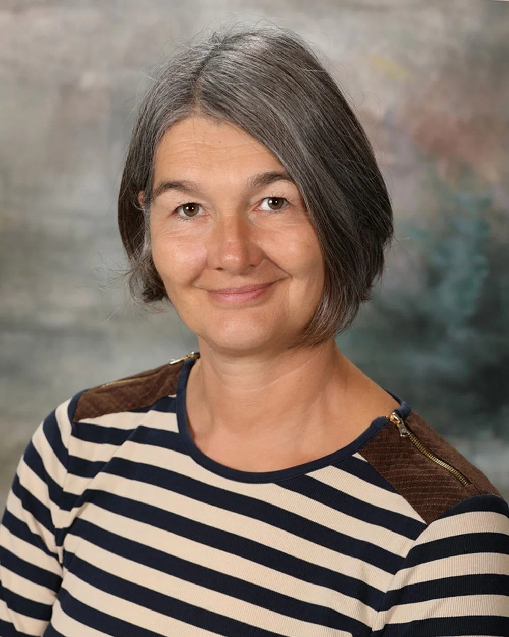 A woman with shoulder-length gray hair wearing a peach-colored T-shirt with a Yellowstone National Park graphic, smiling at the camera.