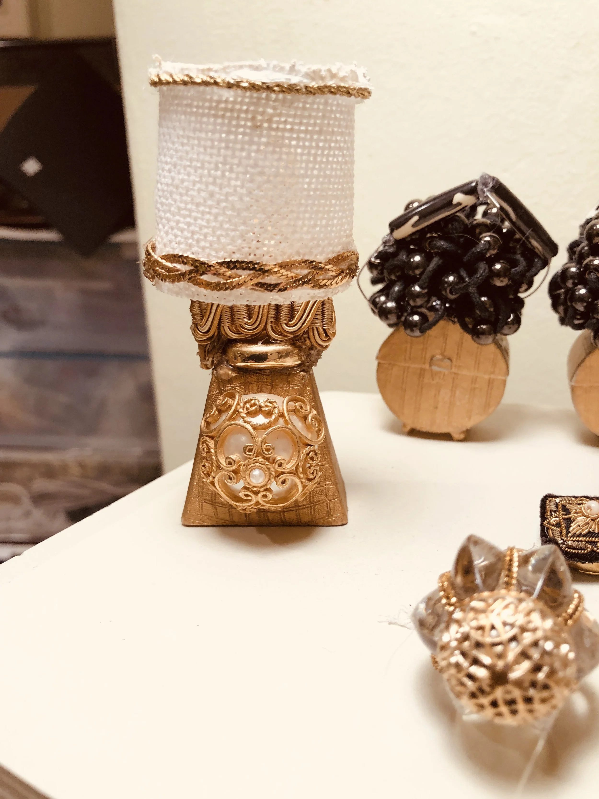 Old jewelry repurposed .Necklace on a stand with a textured, cream-colored ribbon and gold accents, alongside other jewelry pieces.