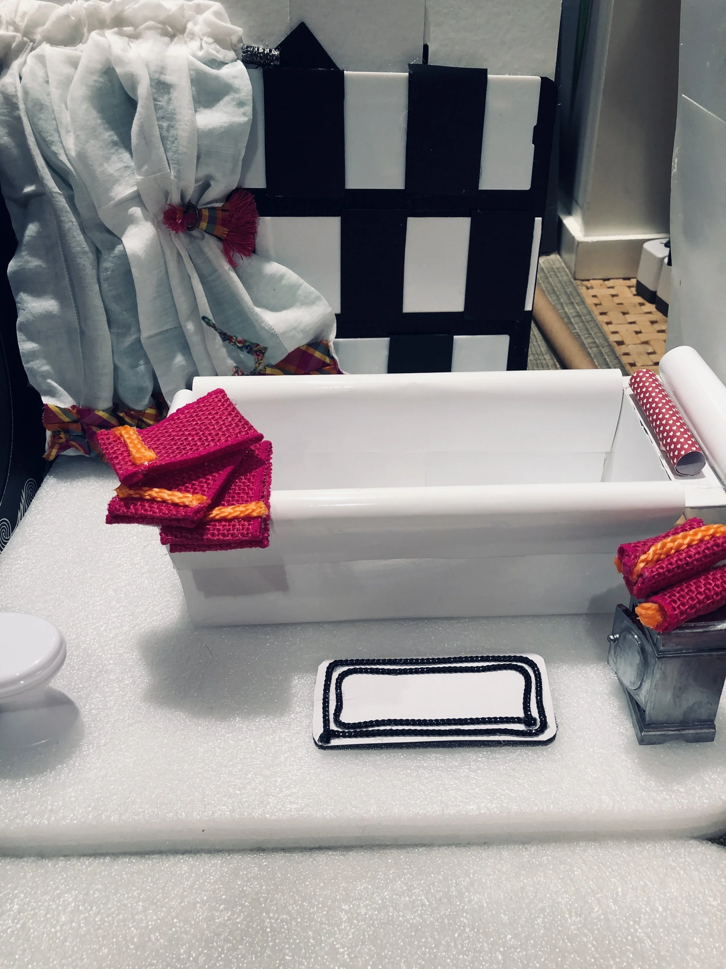 bathtub made from photo paper , pink towels, and fabric with ribbon trim .Tiles made of ribbon over cardboard.