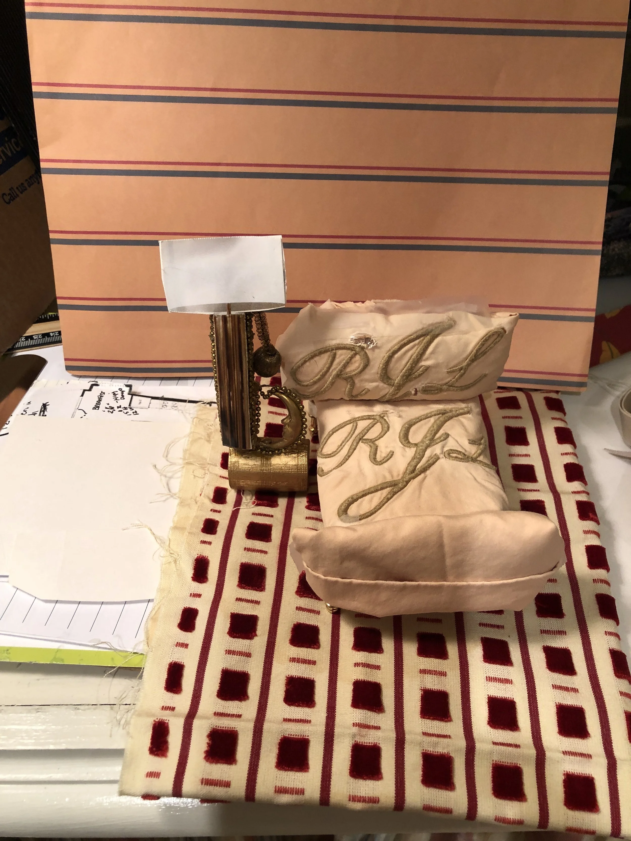 Hand sewn Decorative pillow with initials RJ embroidered on it, a small lamp with a metallic base, and a striped cloth on a table. A replica of her husband's man cave.