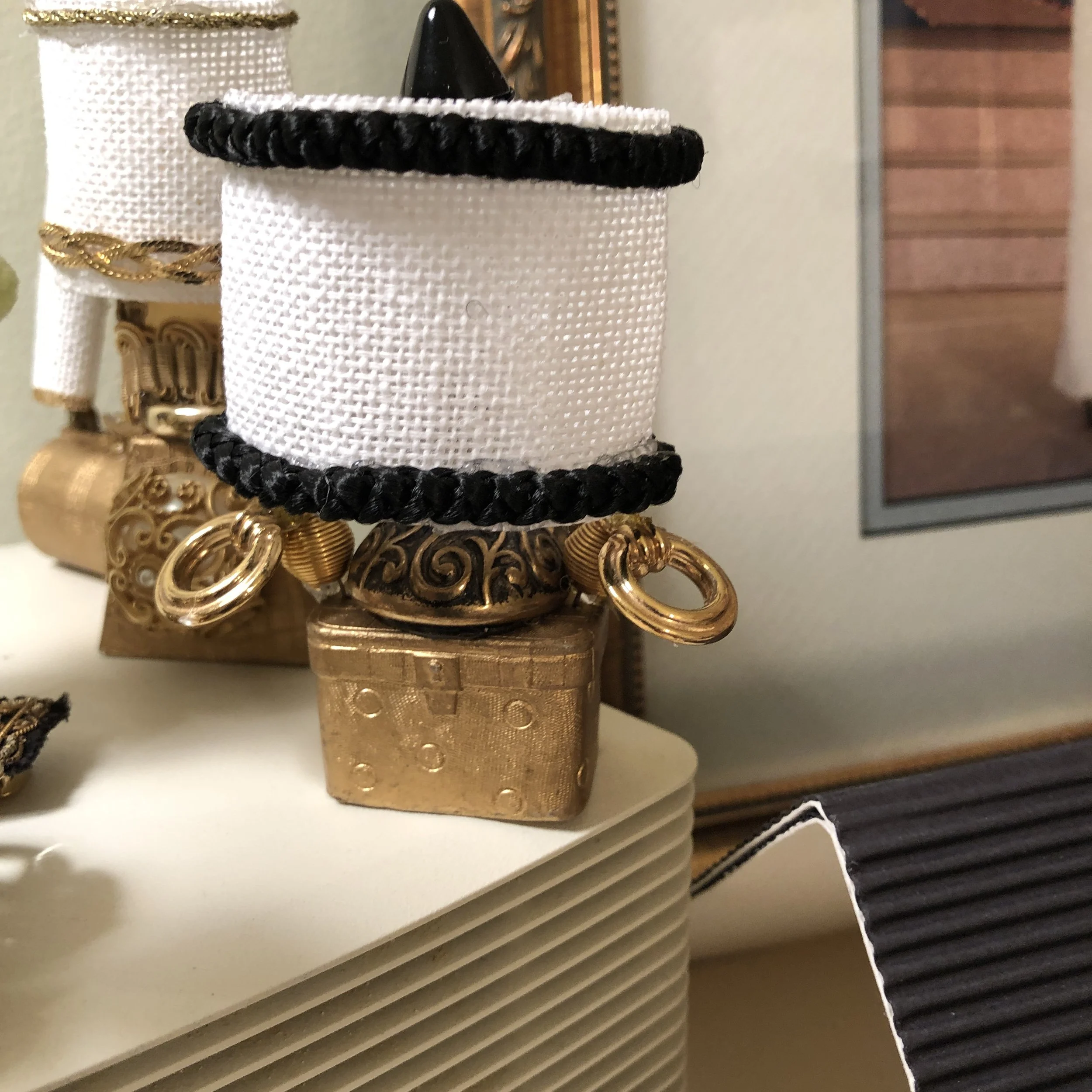 Decorative jewelry display with gold and black ornate jewelry pieces, including rings and chains, on a white textured lamp base.