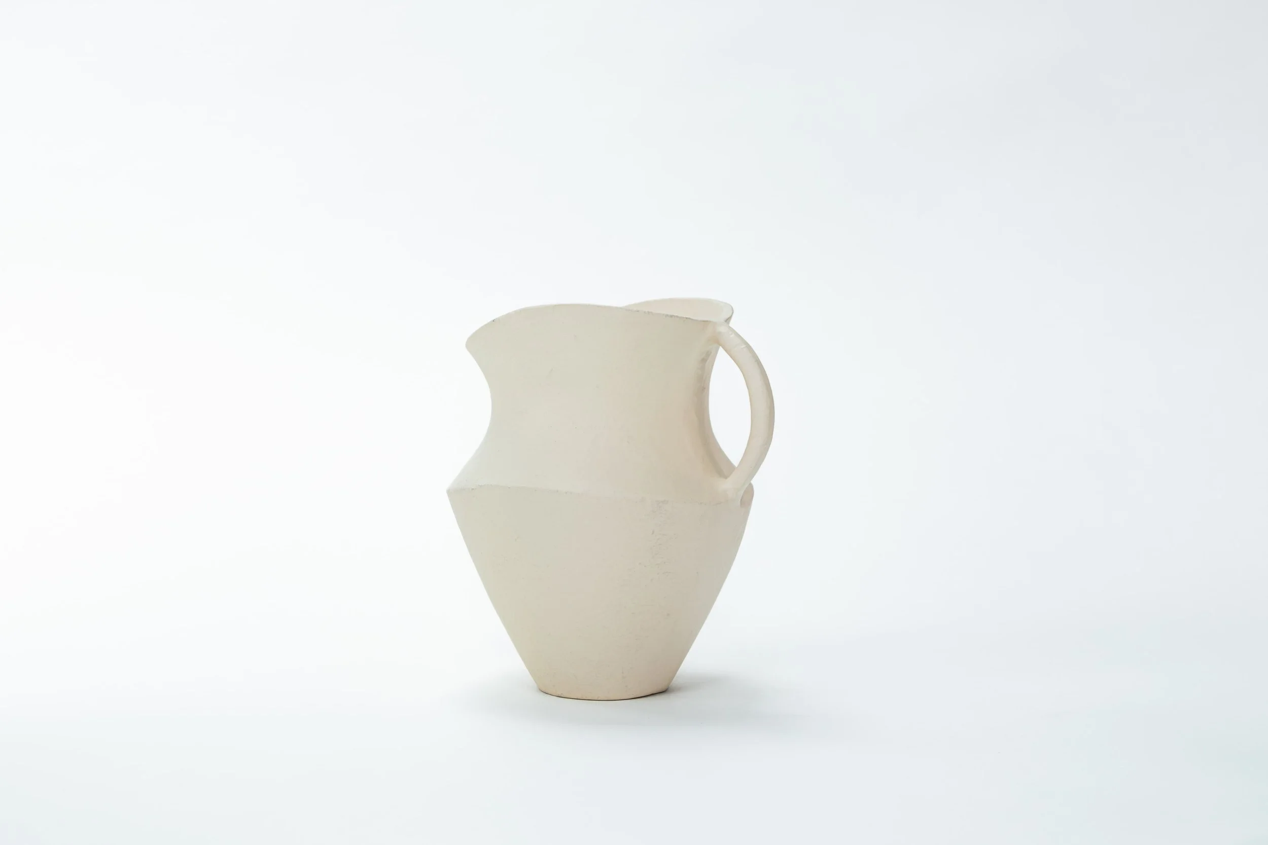 Een wit keramisch vaasje met een abstracte, geometrische vorm tegen een witte achtergrond.