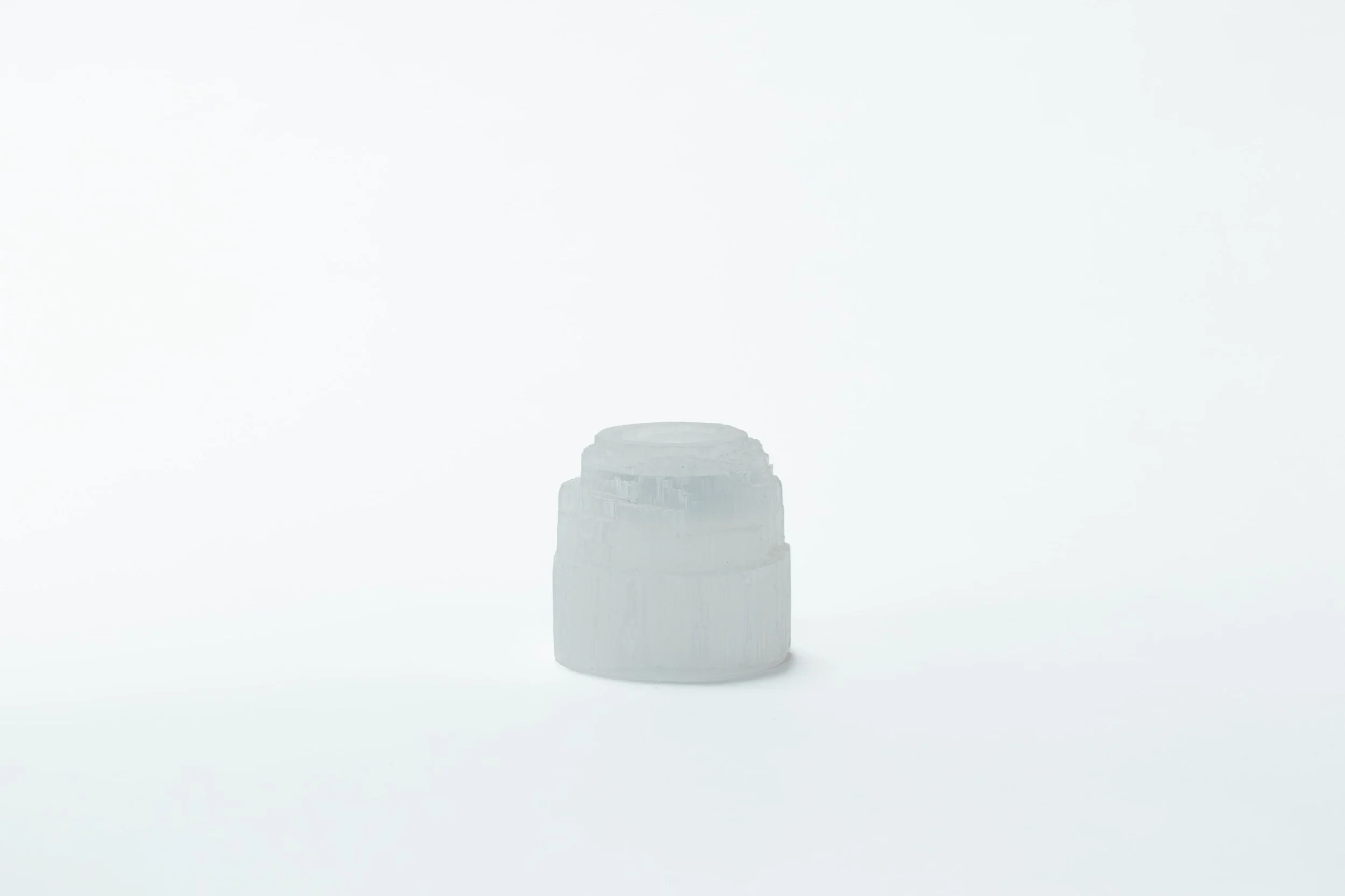 Een wit, ruw gevormd object dat lijkt op een kleine pot of beker op een lege witte achtergrond.