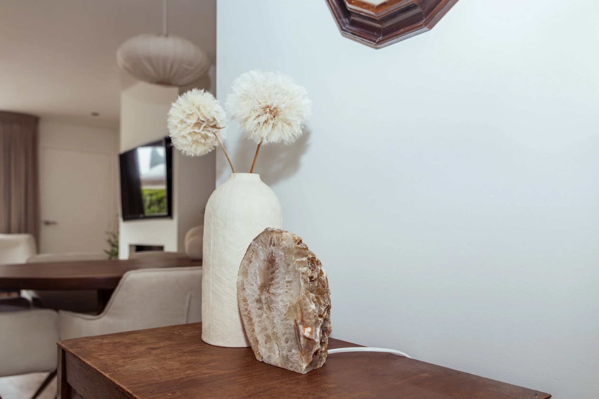 Witte vaas met drie grote bloemkugels en een grote rots op een houten tafel in een moderne woonkamer.