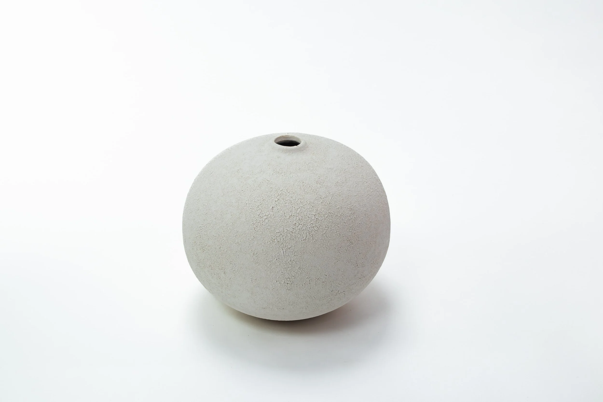 Een witte, ronde keramische pot met een kleine opening aan de bovenkant, geplaatst op een witte achtergrond.