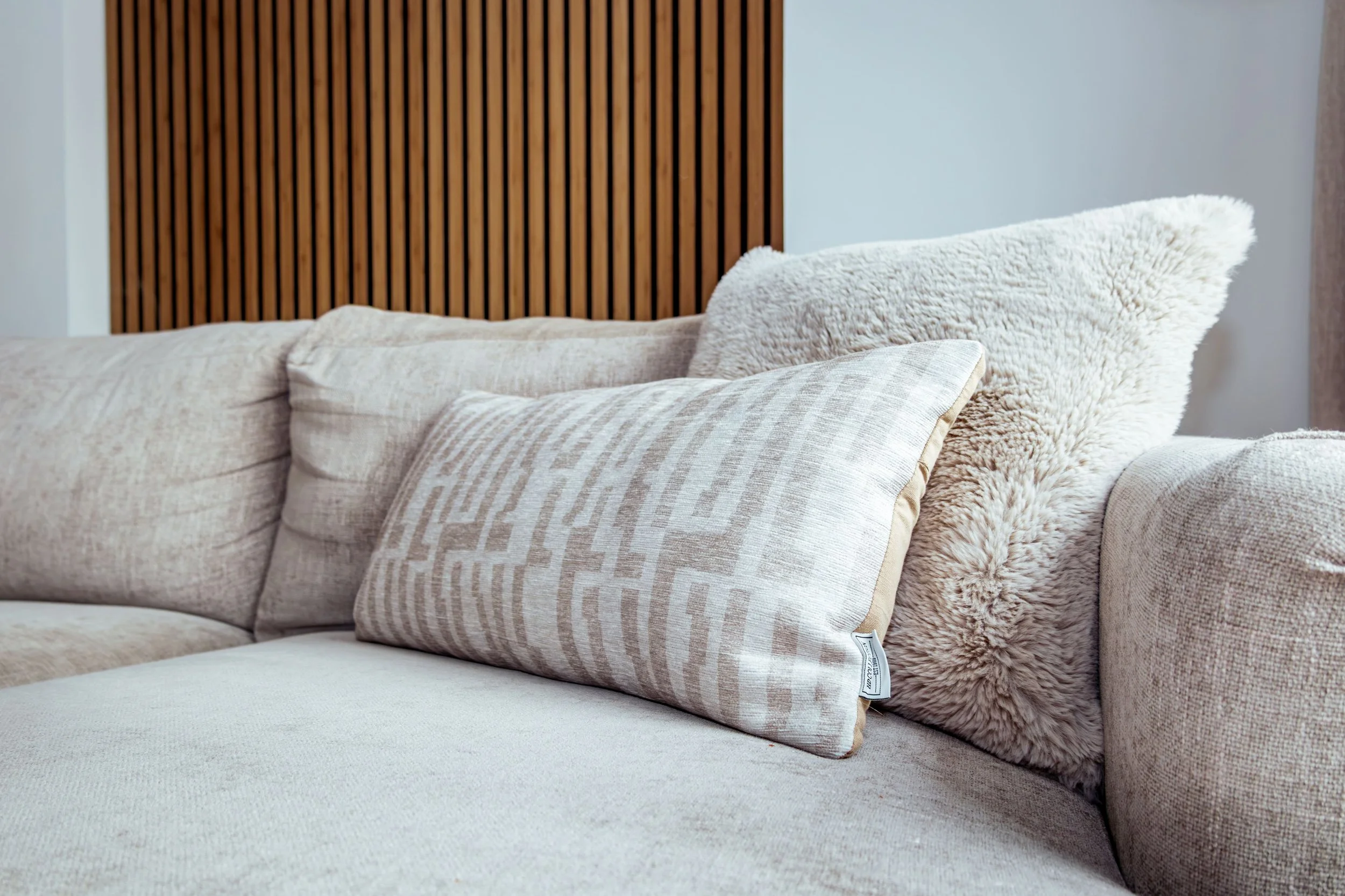 Een bank met verschillende sierkussens, inclusief een zachte, pluizige, crème gekleurde kussen, een rechthoekig kussen met een geometrisch patroon, en een licht beige bank.