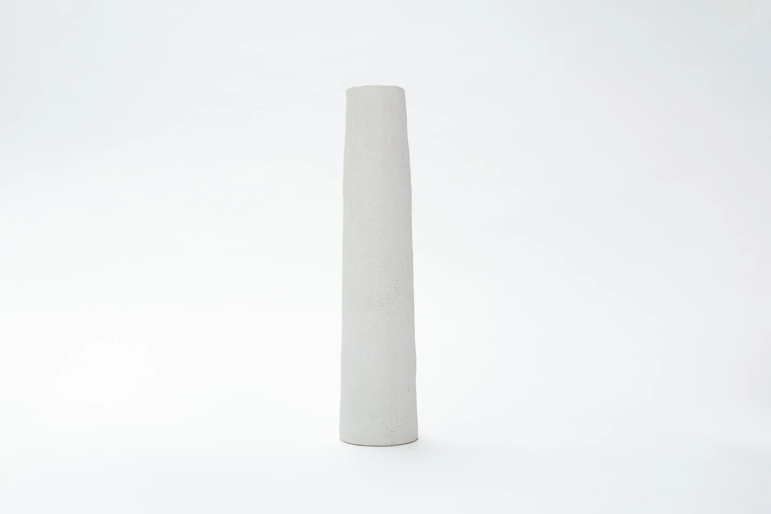 Een langwerpige witte sculptuur met een ruwe textuur, staand op een witte achtergrond.