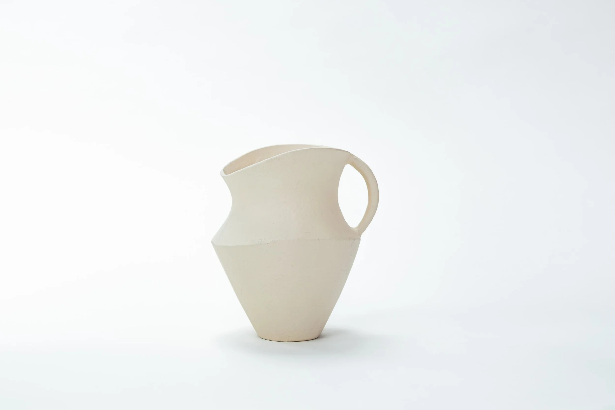 Een wit, artistiek vaasje met een unieke geometrische vorm en een enkele handvat, geplaatst op een witte achtergrond.