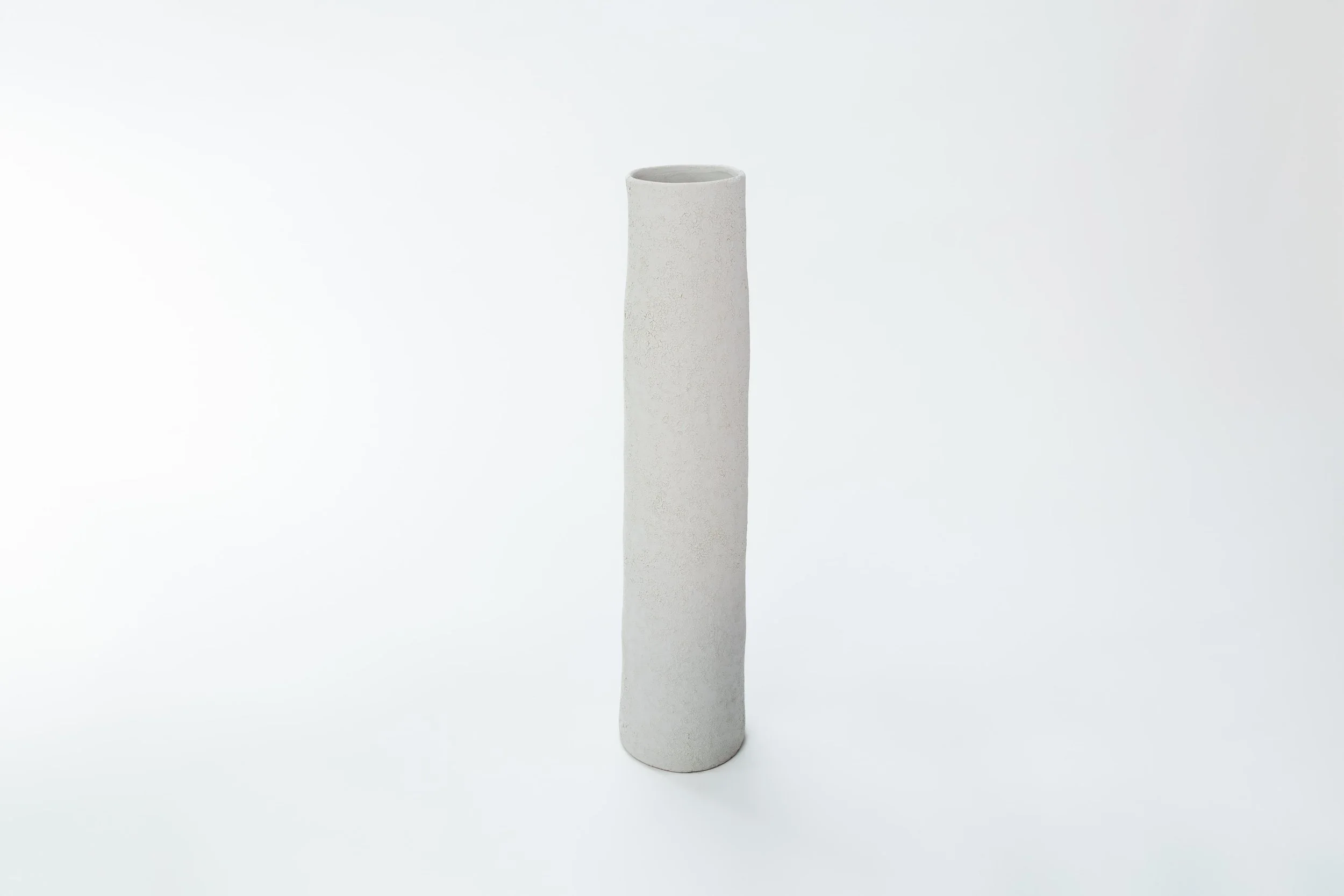 Een witte, langwerpige keramische fles met een uitgestrekt, licht golvend ontwerp, geplaatst op een witte achtergrond.