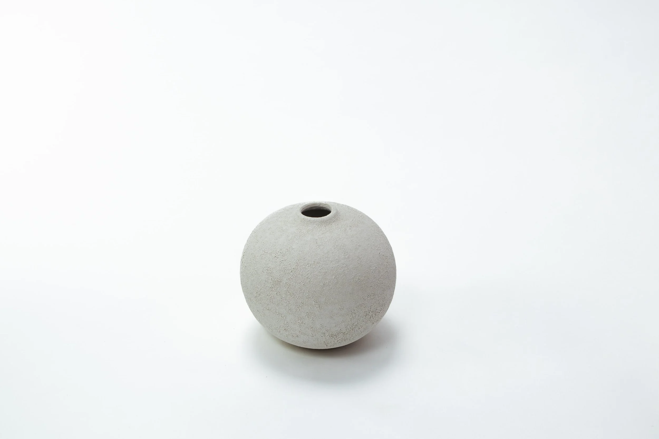 Een ronde, grijze, ruwe keramieken vazen op een witte achtergrond.