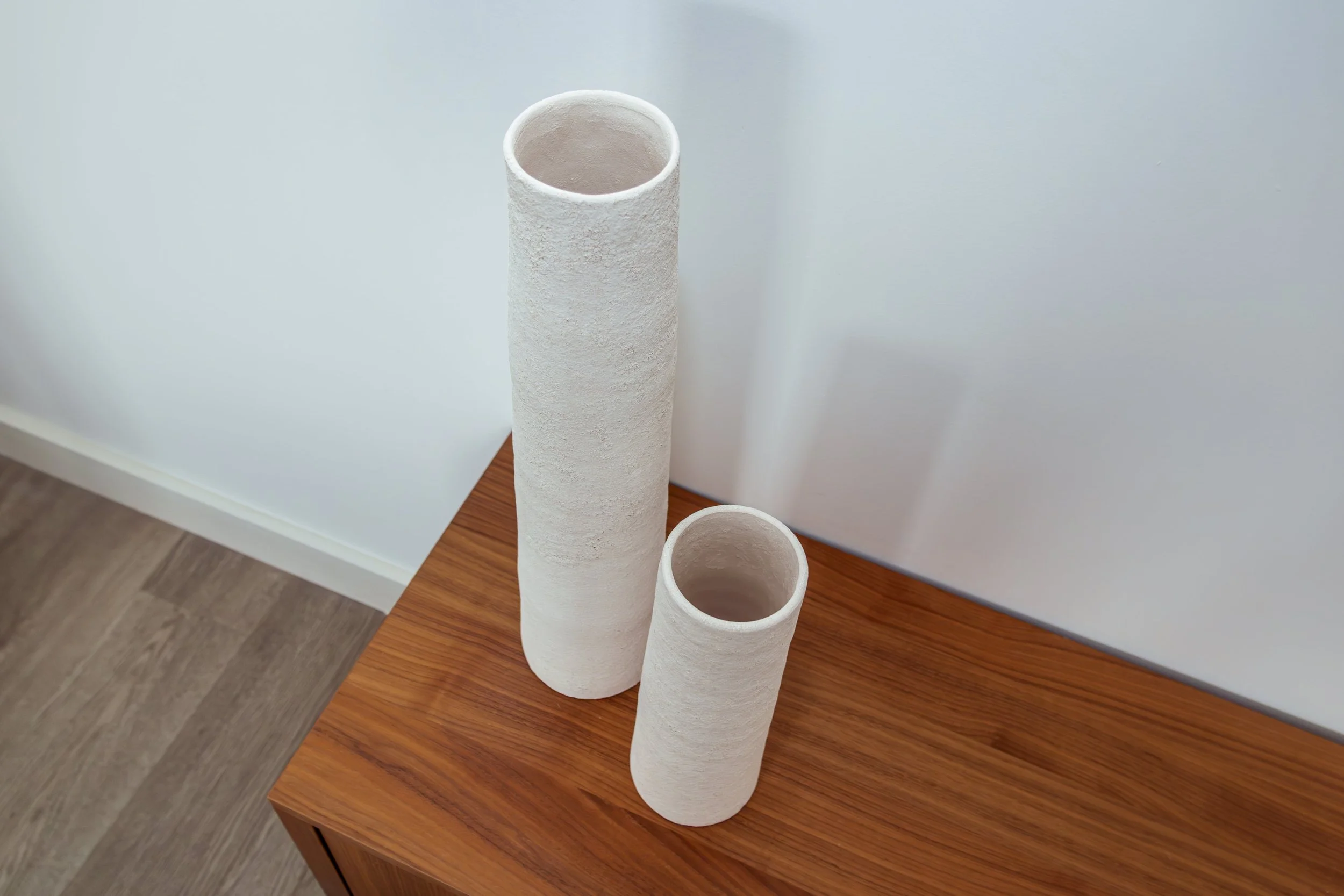 Twee witte keramische vazen op een houten tafel.