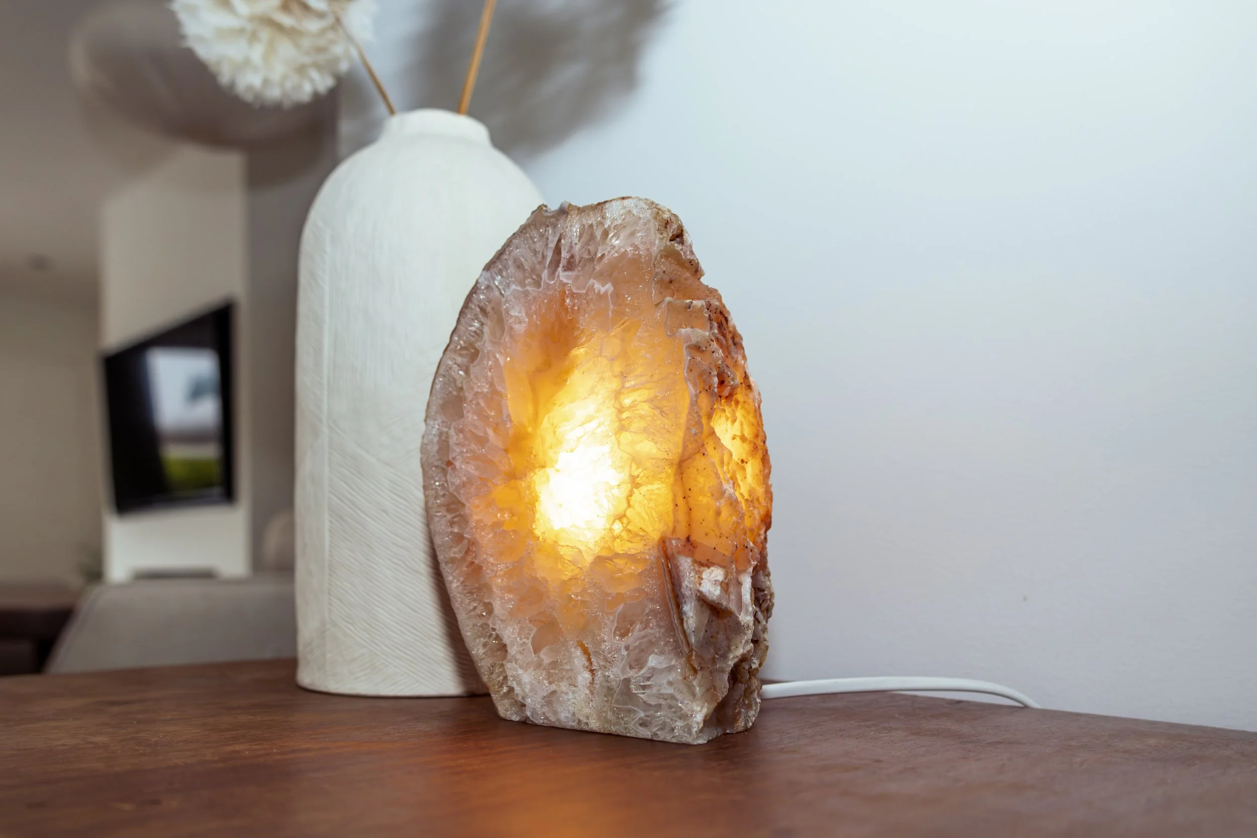 Himalaya zoutlamp op houten tafel met witte muur en decoratief vaasje op achtergrond.
