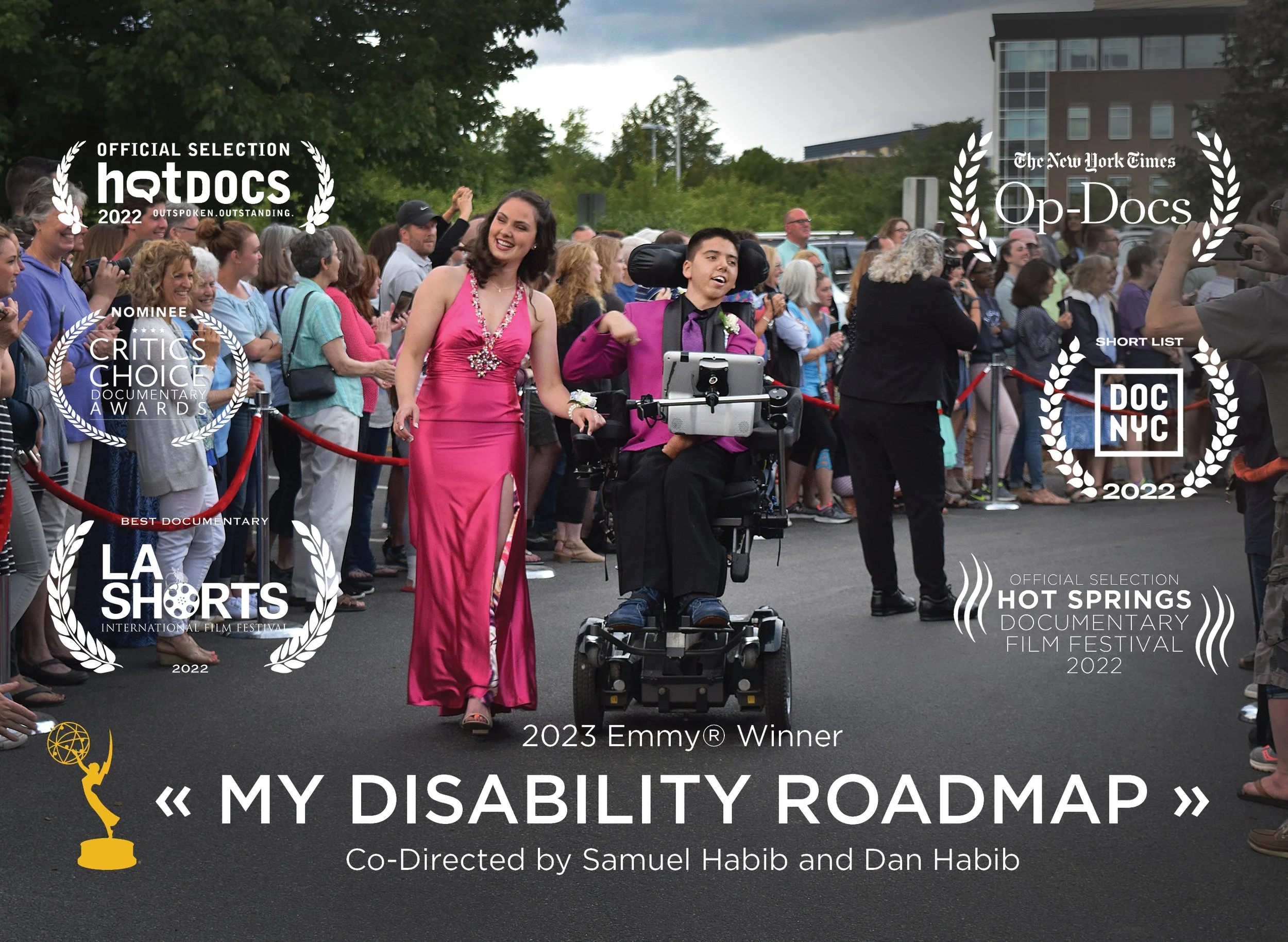 Sam Habib  in a wheelchair being escorted by a woman in a pink dress at a public event with a crowd of people in the background, promoting a documentary titled 'My Disability Roadmap'.
