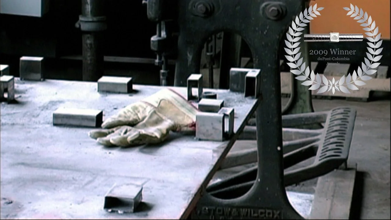 A dusty, abandoned industrial setting with a rusted bench, a pair of work gloves, and metal blocks on a concrete floor.