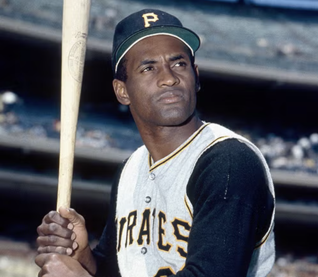Roberto Clemente in a Pittsburgh Pirates uniform and cap holding a bat, looking off into the distance.
